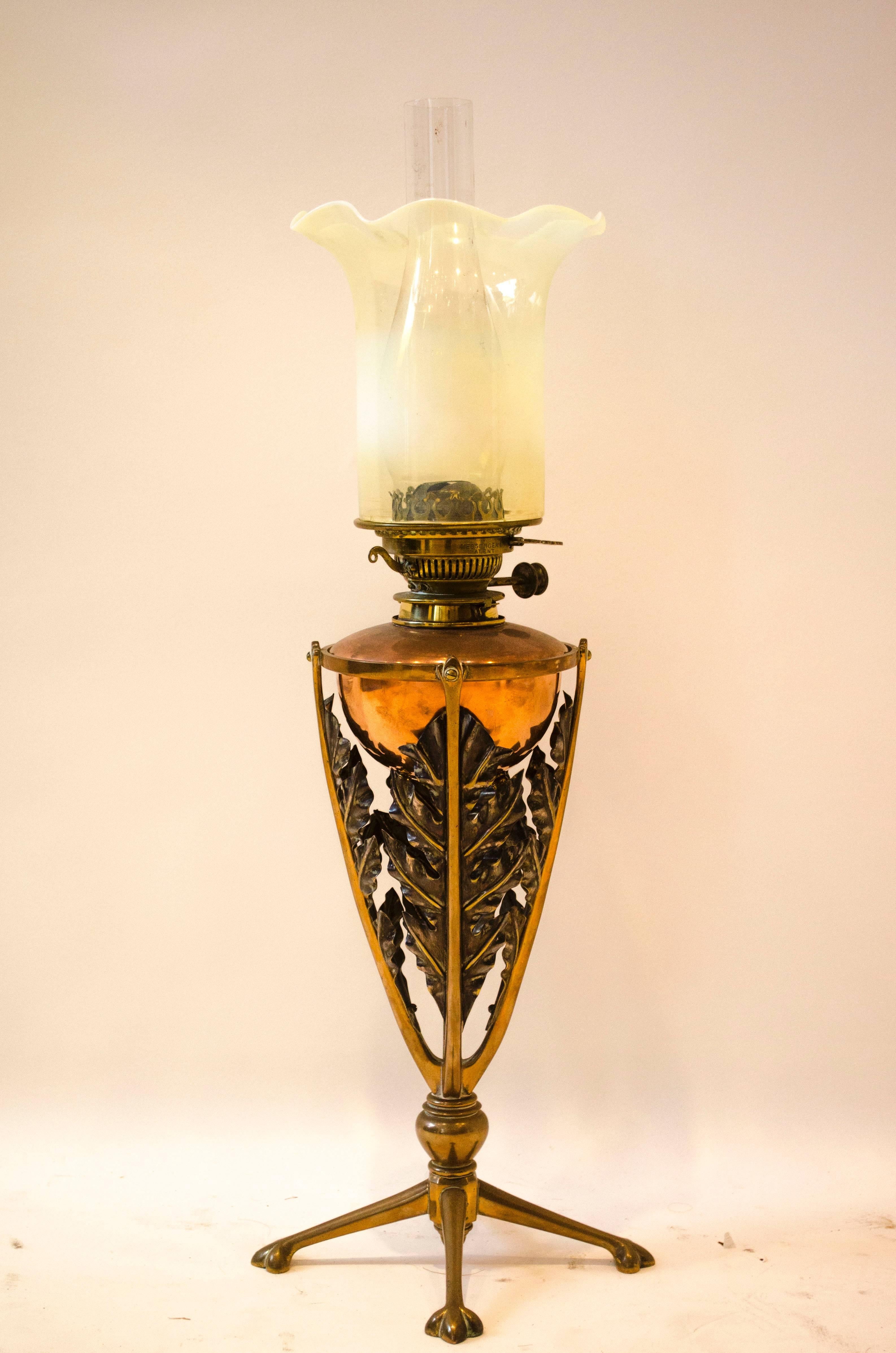 W.A.S. Benson. A brass and copper oil lamp with stylized leaf detail within a conical base, stood on four splayed feet.
Peacock shade sold separately to lamp-display only.