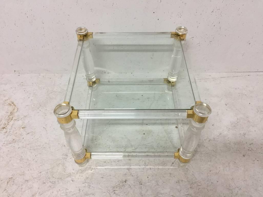 A French Lucite square two-tier side table on curvaceous legs with brass details that unite the legs stood on little turned cap feet.
