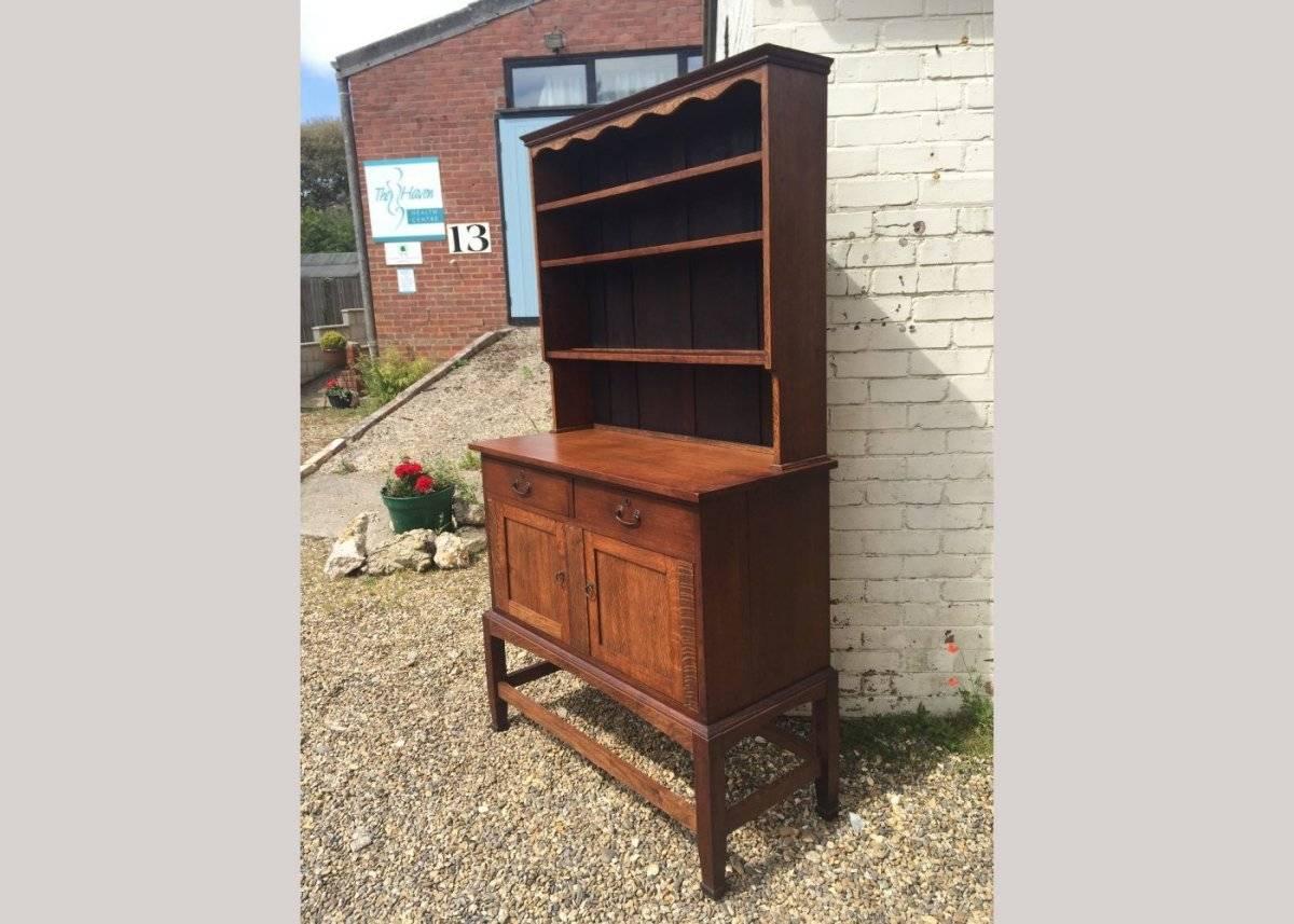 An excellent quality Arts and Crafts two-door oak dresser with a decorative shaped top, cascading upper shelves, and a sweeping arched apron on four square legs united by side stretchers.