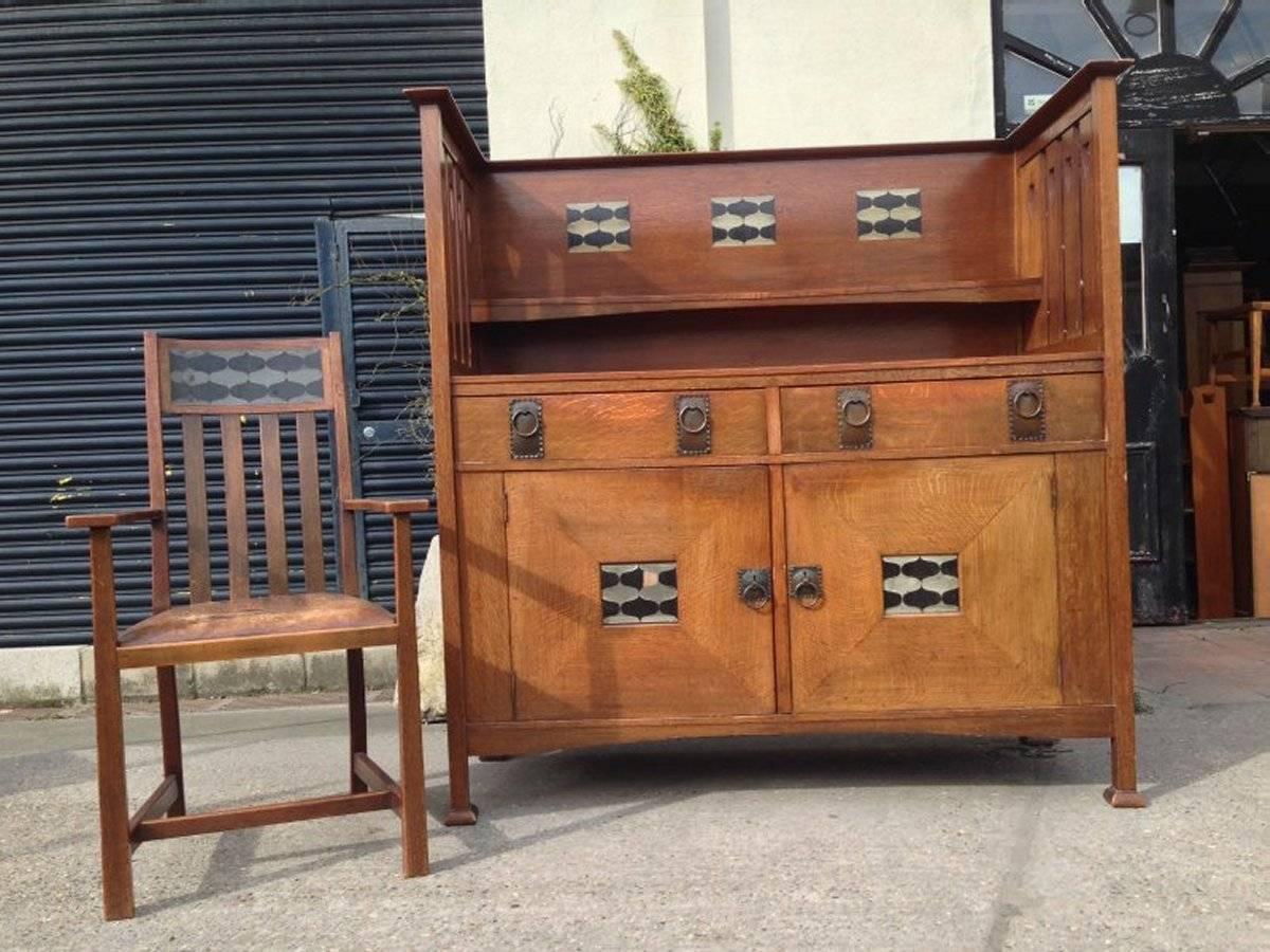 George Montague Ellwood, made by Bath Cabinet Makers,. An Arts and Crafts oak sideboard and eight matching dining chairs  The sideboard with elongated slatted sides with heart cut-outs and stylized ebony and pewter inlays to the back and to the