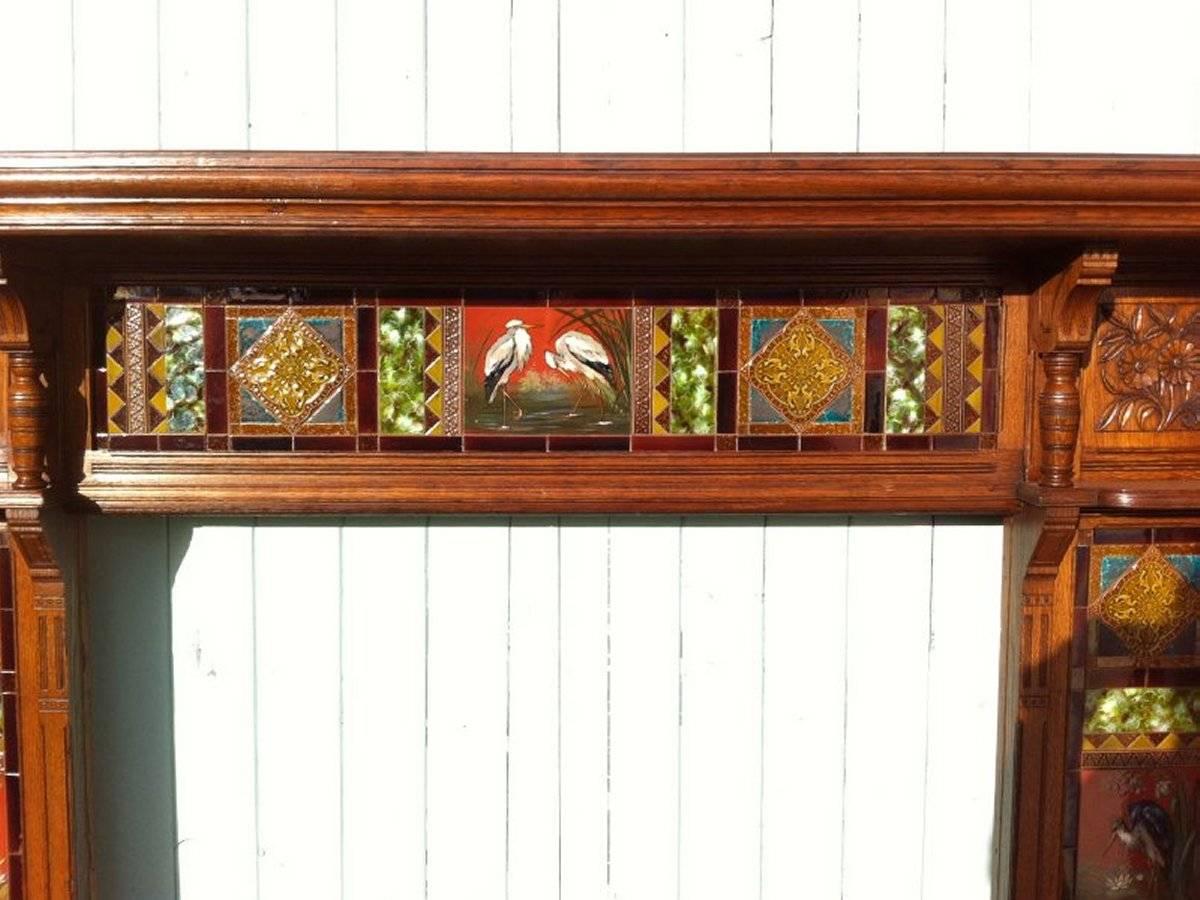 An impressive Gothic Revival oak fireplace surround attributed to Bruce Talbert with carved floral details to the top sides with turned supports with stunning hand-painted tiles attributed to Mintons (AJS?) depicting cranes and wading birds in