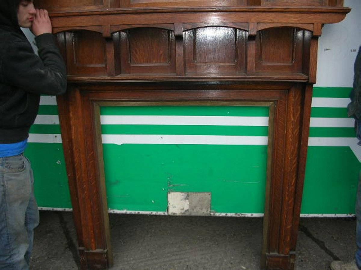 Liberty and Co, an impressive Arts and Crafts oak fire surround with two upper cupboards set with green tinged stained glass doors with iron ring pull handles. Brass molding to the fireplace opening. Original enamel label to the back.
Measures:
