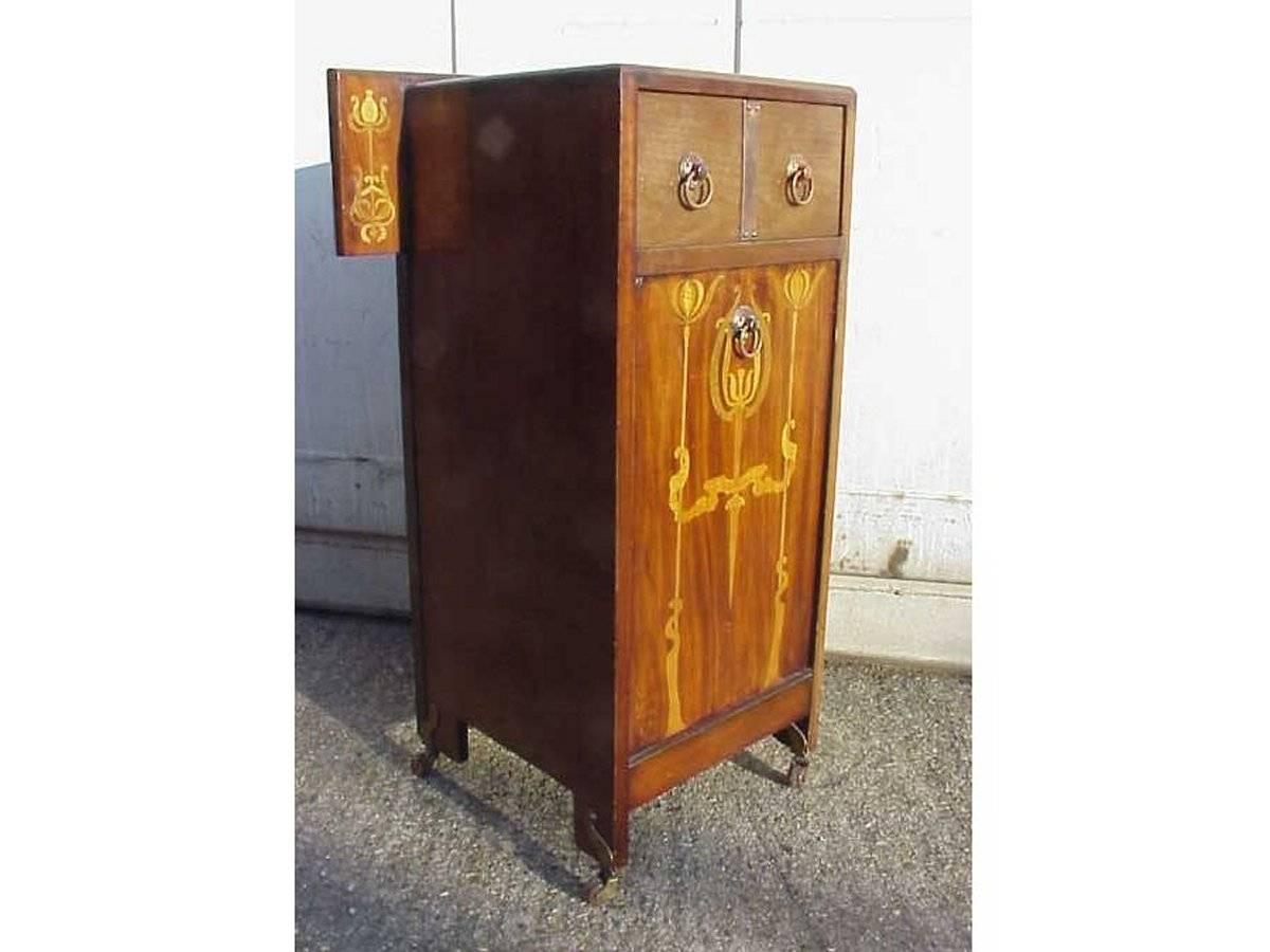 An Arts & Crafts coal/log purdonium attributed to Liberty and Co with inlaid stylized floral details to the upper wings and to the front with two handy upper drawers and pull down coal box retaining the original liner, stood on brass stylized floral