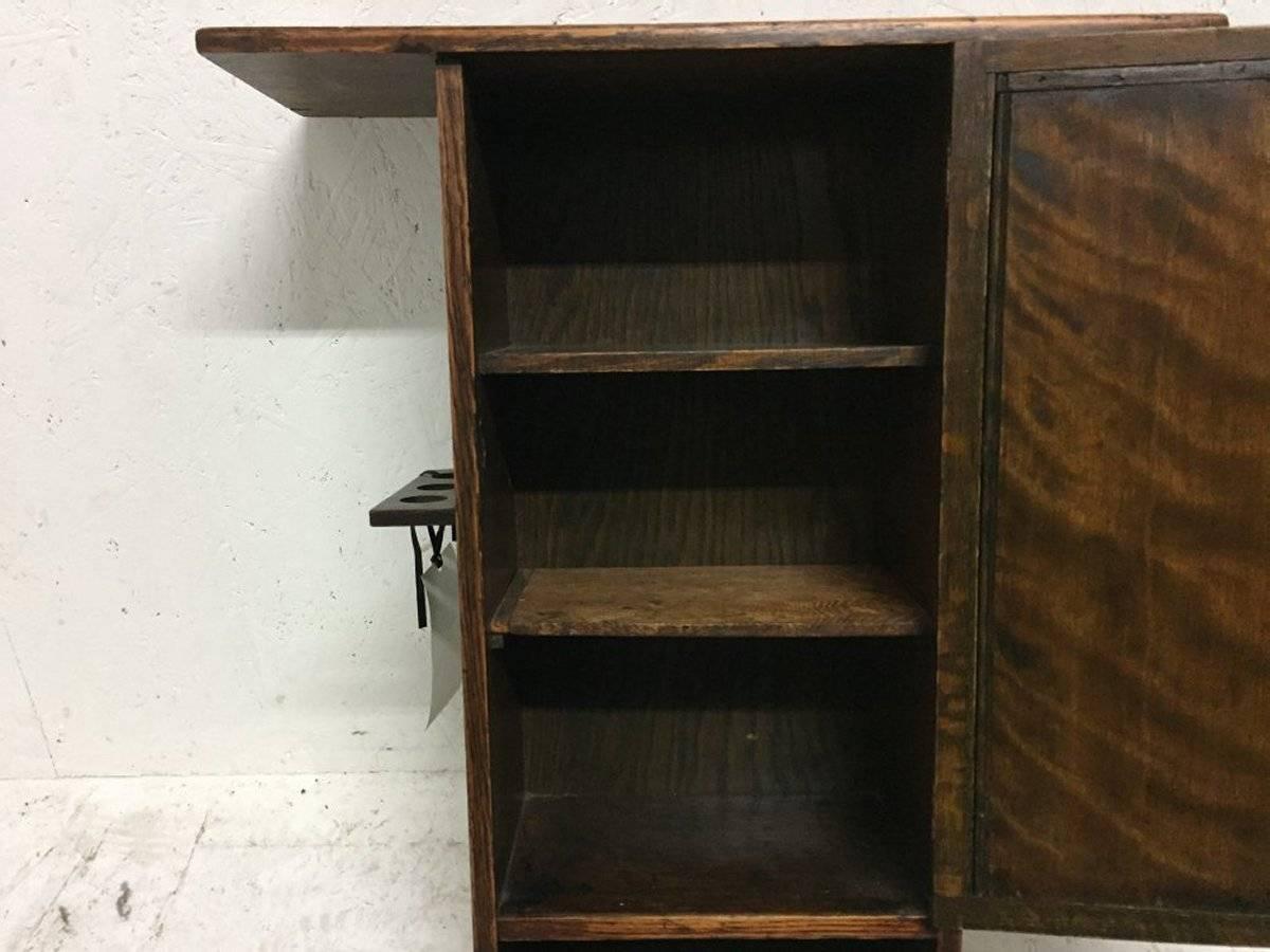 Liberty & Co., an Arts & Crafts oak smokers wall cabinet decorated to the door with a gentleman smoking a pipe. It has a groove to the top for displaying a large decorative dish with pipe holders to the sides.


Measures: Height 27 1/2