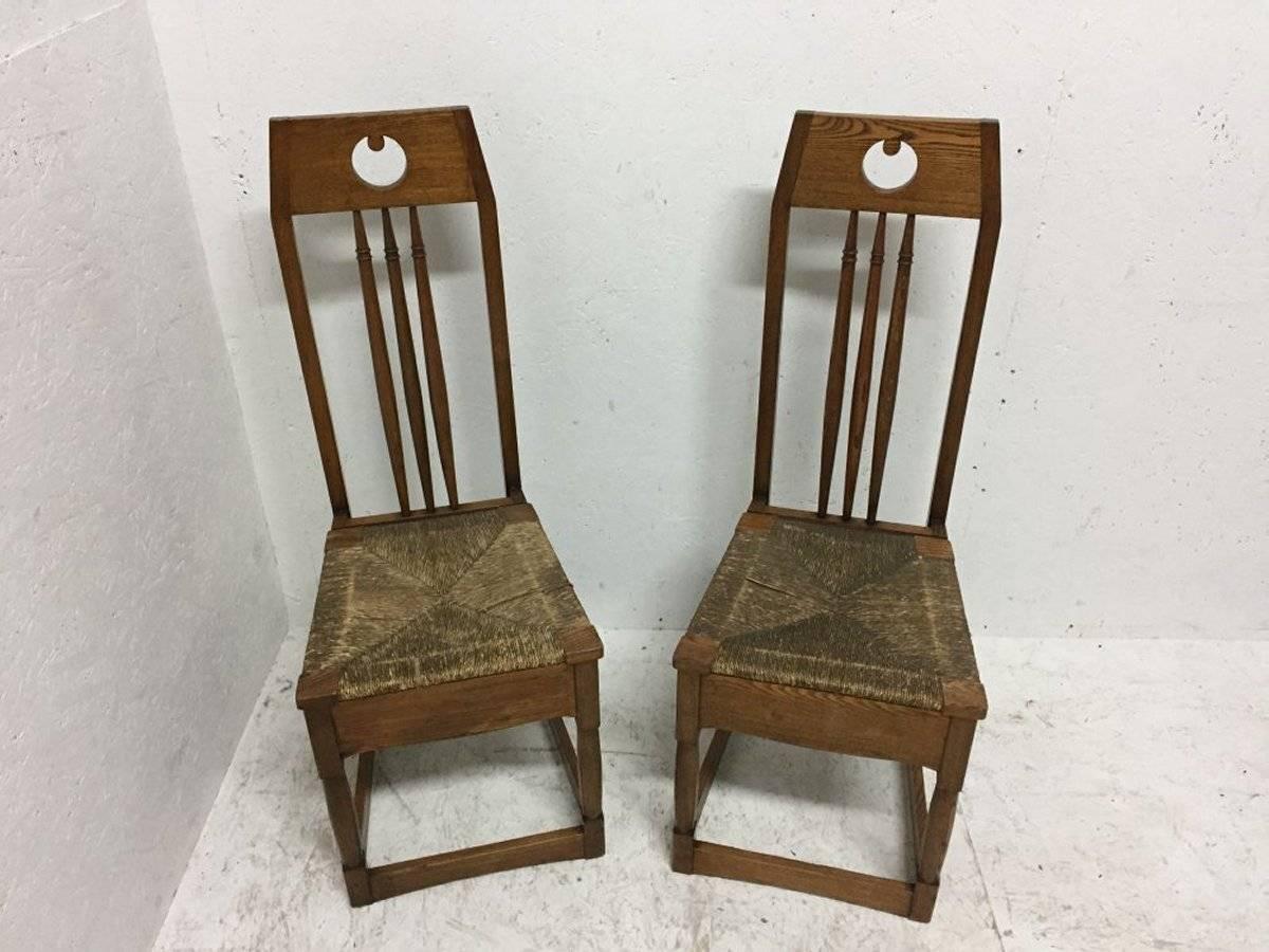 Shapland and Petter, une paire de chaises latérales en frêne dans le style de M H Baillie Scott avec des découpes circulaires stylisées, des dossiers en fuseau, des sièges en jonc d'origine et des traverses de sol façonnées.