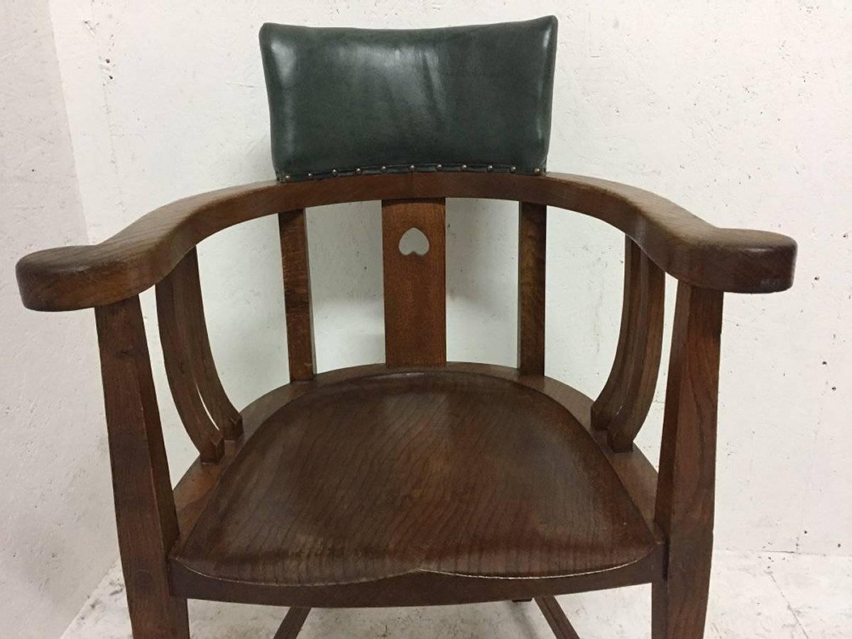 E A Taylor attributed. An Arts and Crafts oak tub chair with a single pierced heart to the back support and shaped supports below the arms, the shaped backrest with leather and a shaped seat.