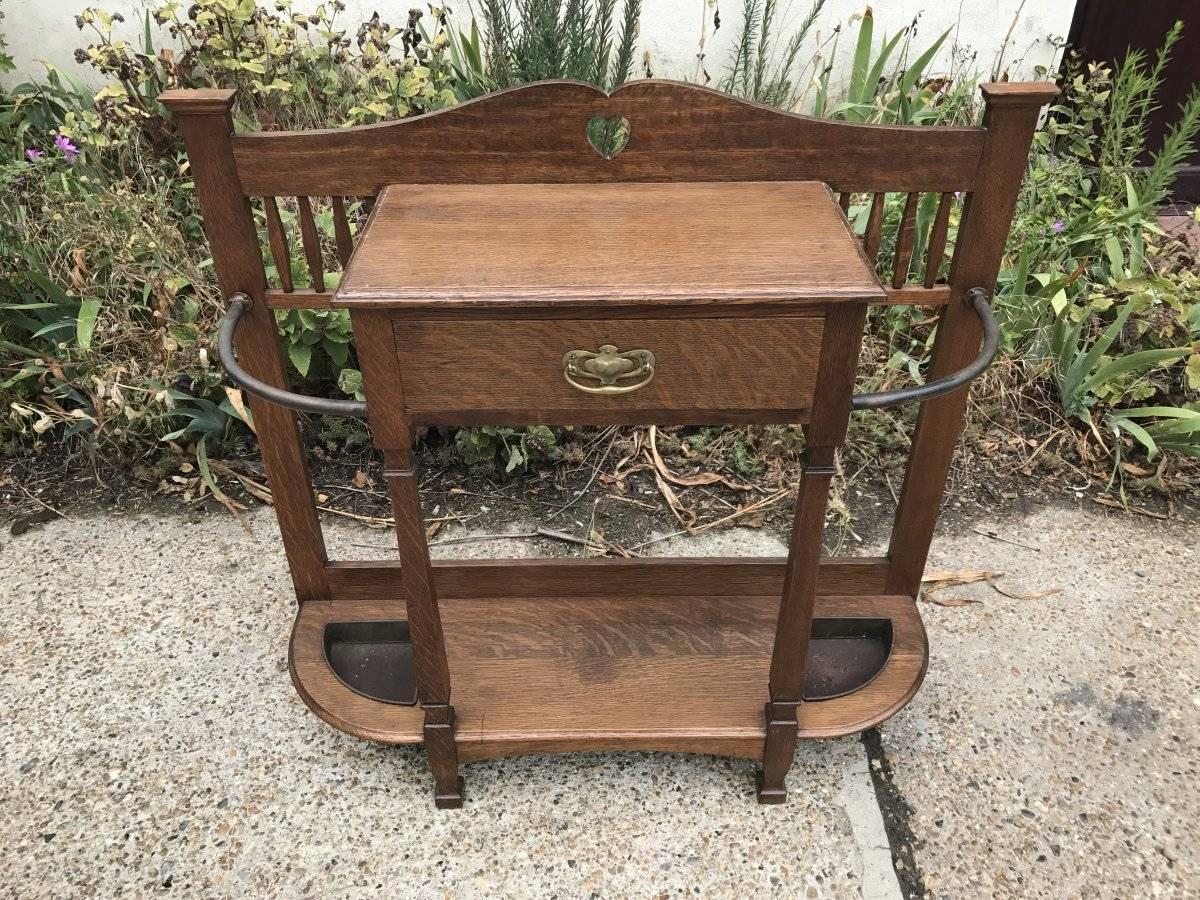 Shapland and Petter Arts & Crafts oak stick stand with pierced heart detail to the top a single upper key and glove drawer with stylized brass handle flanked by a pair of umbrella stands to each side. It does have the original tin drip trays