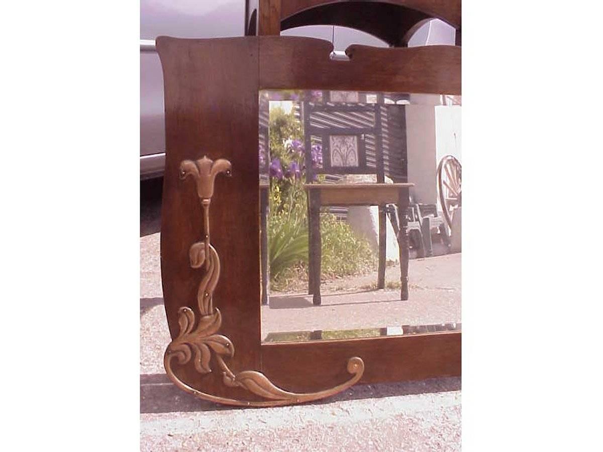 An Arts & Crafts shaped oak bevelled mirror with stylised floral copper details with crescent style cut-outs to the top.