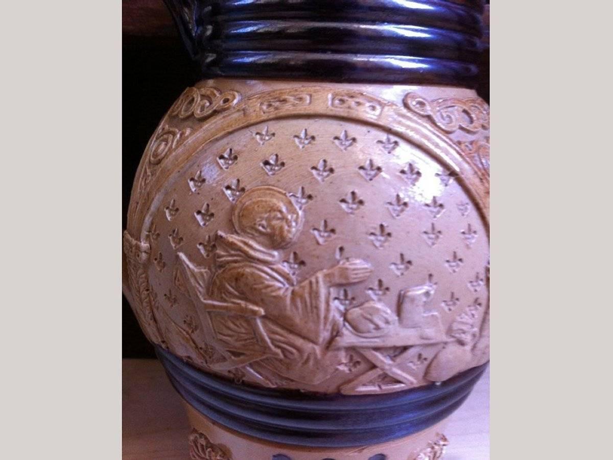 Un Royal Doulton Lambeth. Rinascimento gotico. Una brocca comica che raffigura un monaco in tre scene che mangia la sua cena e si ubriaca
Nella prima scena il suo piatto è pieno e sta iniziando a mangiare il pollo arrosto e a bere. C'è un uccello