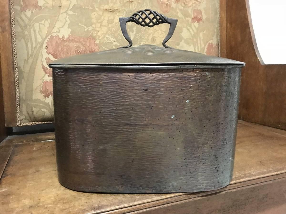 Guild of handicraft, attributed A super quality Arts & Crafts hand-hammered oval copper bread or storage bin with a stylized twisted blacksmiths made iron handle rising from stylized floral decoration to the lid. Retaining the original patina.
  