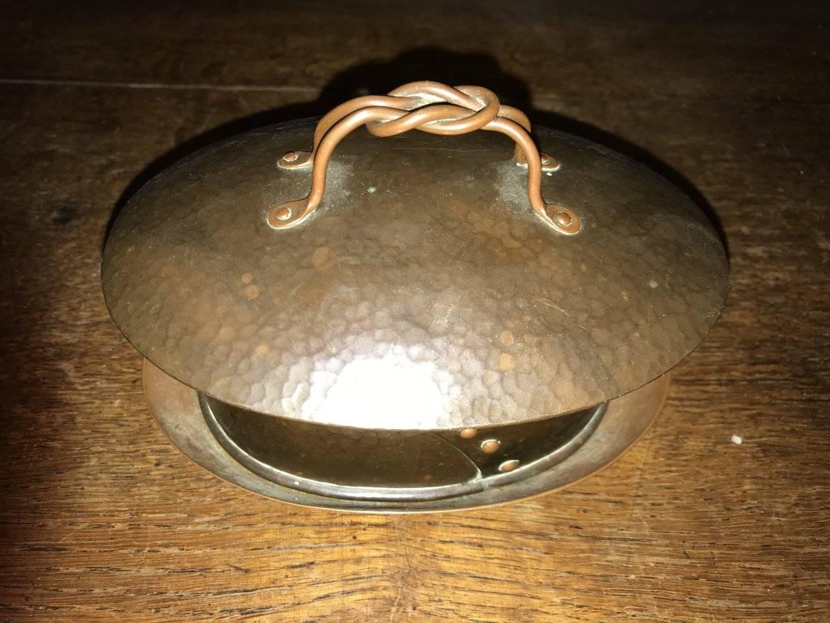 Guild of handicraft, attributed. An arts & crafts hand-hammered copper butter dish and tray with the original porcelain liner. The lid with a hand twisted copper wirework handle and riveted details to the side.
Retaining original patina.