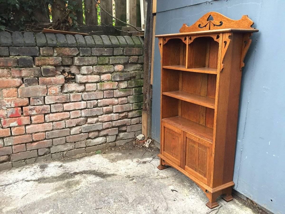 A very good quality Arts & Crafts oak bookcase with pierced stylized floral, heart details with an inlaid cupboard below.