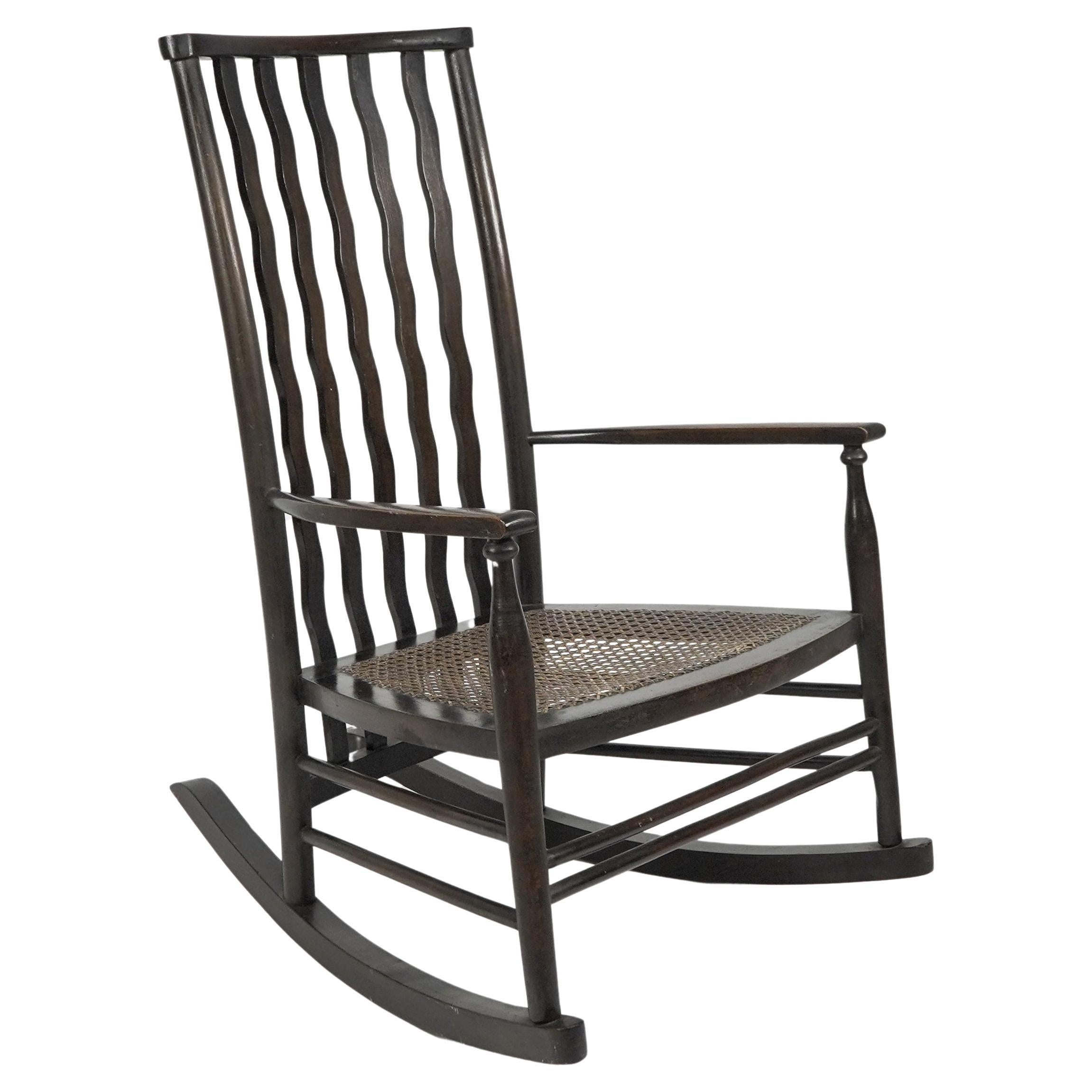 Liberty and Co. A litte beech stained and original cane seated rocking chair For Sale