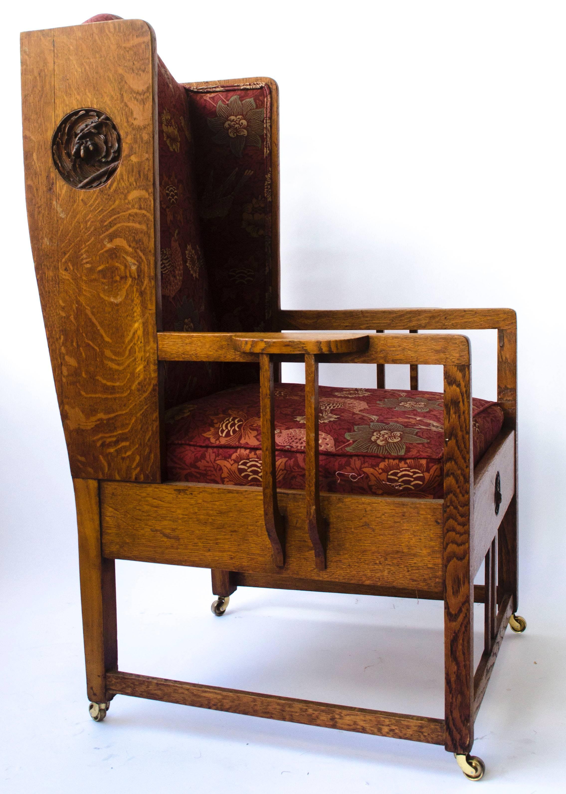 Attributed to GM Ellwood, for JS Henry. 
An Arts and Crafts oak wing back armchair with wonderful life size acorn and oak leaf carved roundels to the front and to each side, highly stylised shaped supports to the armrests and professionally re