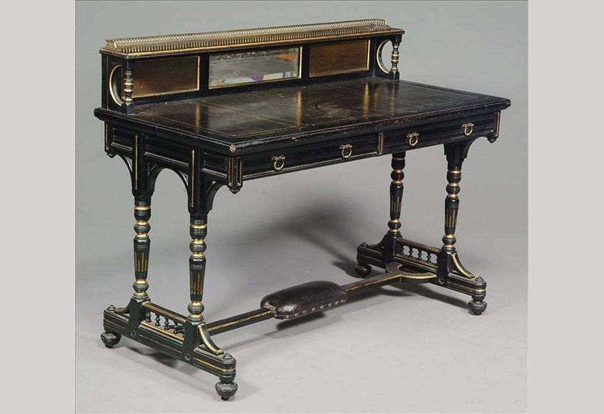 Bruce Talbert attr, made by Gillows and Co of Lancaster.
Aesthetic Movement ebonised and parcel gilt desk.
The upper shelf surmounted by a brass gallery, with a small central bevelled mirror and a black leather writing area with gilt tooling to the