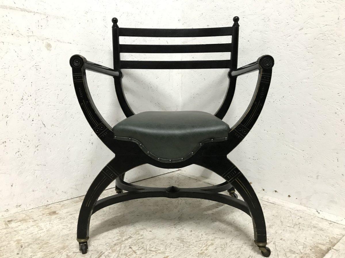 Richard Charles (1823-93), an Aesthetic Movement ebonized elbow chair, circa 1866, with ball finials, a ladder back, later leather seat, gilt highlights and X-frame base with X-frame stretcher, on casters, 83cm high. The attribution is based on the