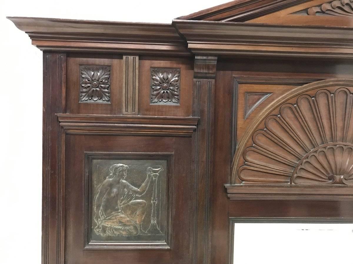 An Arts and Crafts mahogany overmantel in the manner of George Jack with exceptional carved details central bevelled mirror and wonderful hand formed copper panels by James Smithie depicting scantily dressed Maidens, signed JS '96. James Smithie