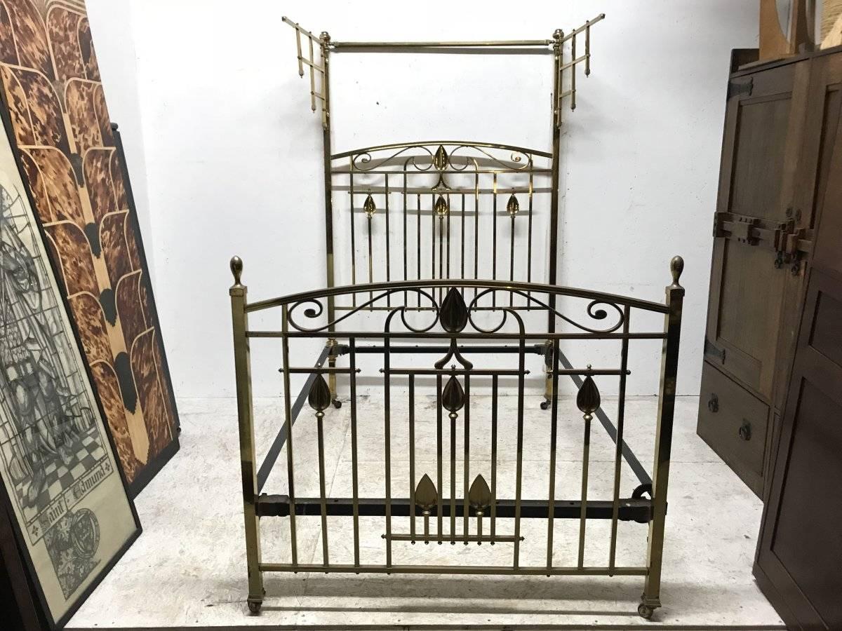 An Arts and Crafts lacquered cast brass half tester double bedstead, with stylised plant and floral details to the head and foot board. With lattice swing brackets to the sides for hanging fabric with a thinner brass rod behind the very top rail to