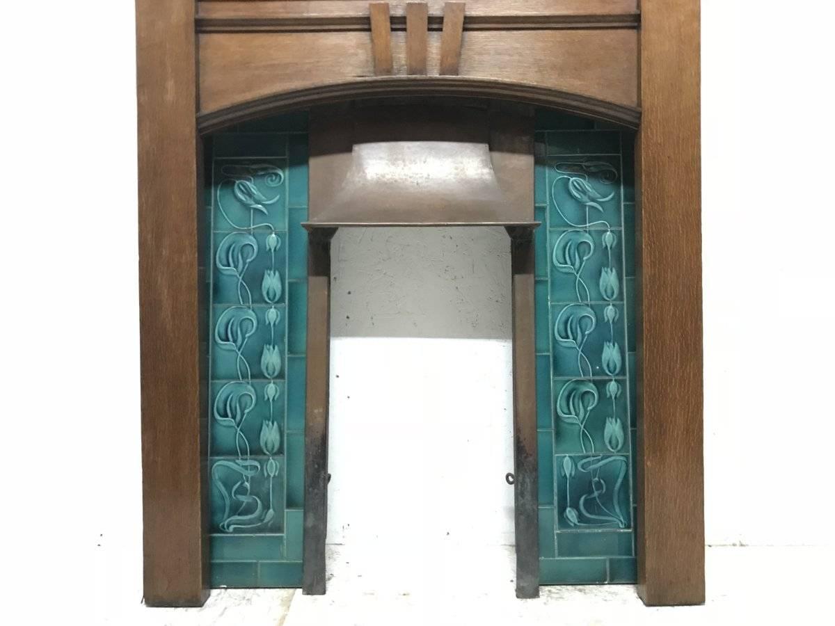 A complete Arts & Crafts oak fireplace in the Liberty style with three arched upper details, complete with it's original Turquoise floral tiled insert with a detachable copper hood. 
Ready to install. 
Measures: Height 68 1/2
