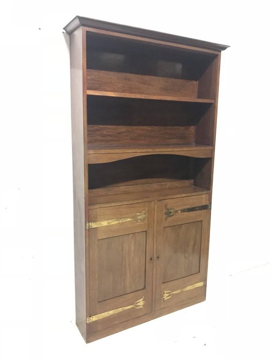 Liberty & Co. A Slim Arts & Crafts walnut bookcase with open upper shelves and cupboards below with stylised brass hinges.
Measurements are to the cornice.
