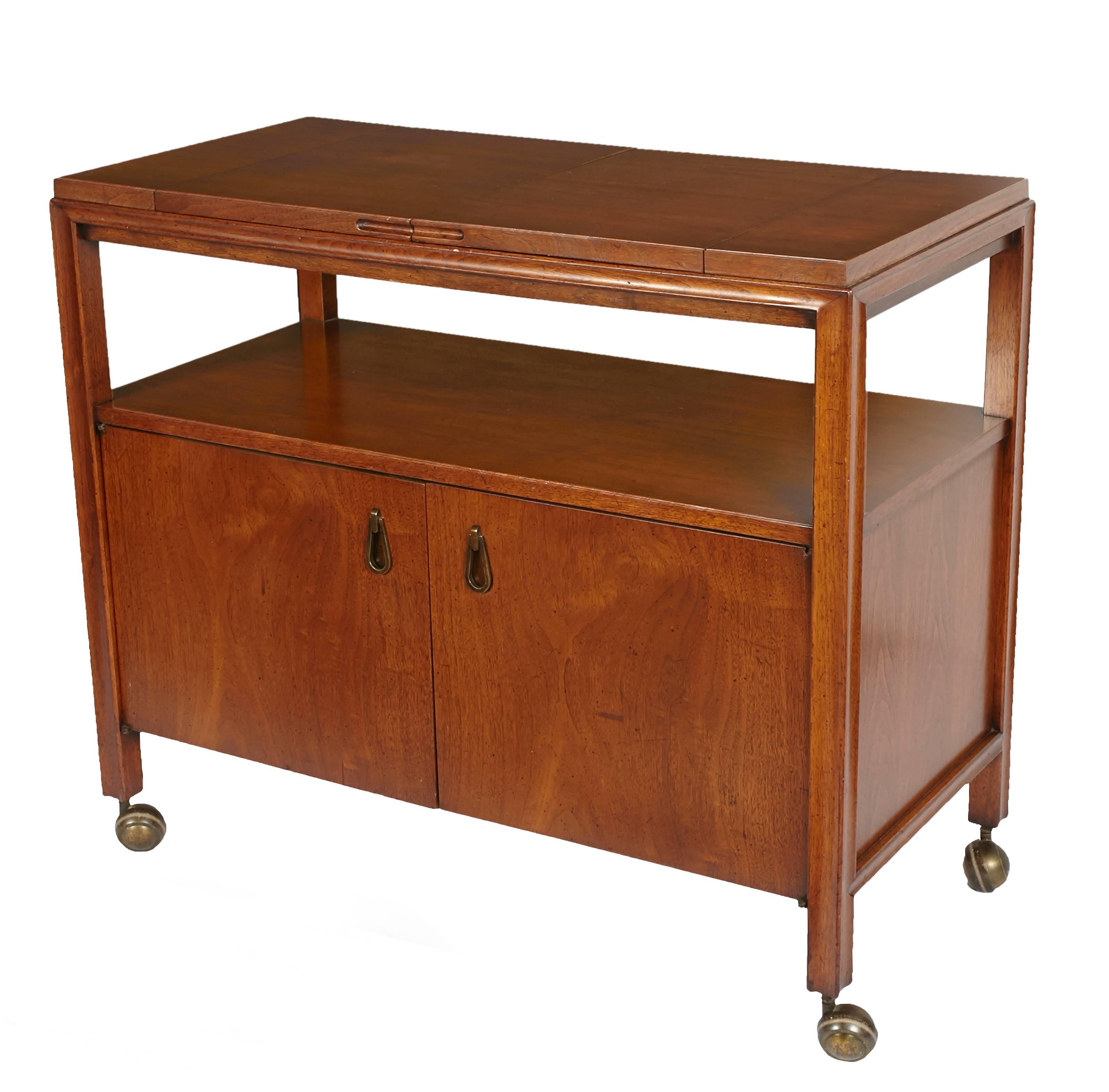 Beautiful Mid-Century Modern Walnut bar cart or server with brass handles and brass casters.
Top opens up with a black laminate top. Cabinet opens up with one shelf.
Has been lightly restored and is in beautiful condition.