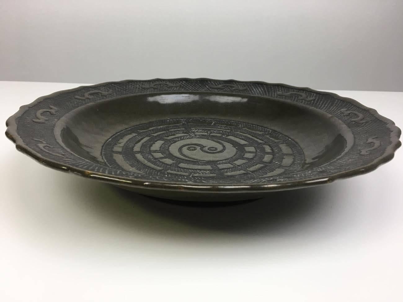 A very stunning glazed Chinese porcelain plate which features geometric patterns and a yin-yang symbol in low relief. The plate's faintly iridescent green color is apparently due to a very unusual and rare tea dust glaze. The charger/ plate was