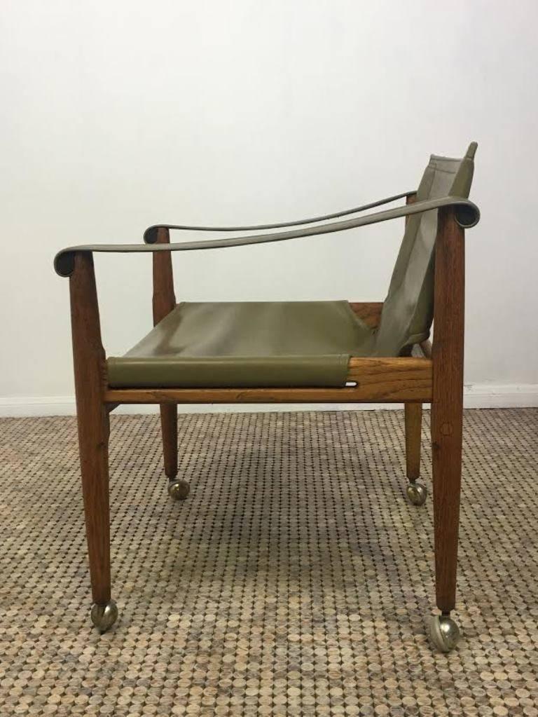 Vintage Mid-Century Modern brown Saltman safari chair designed by Douglas Heaslett in solid oak frame with khaki leather sling arms and seat. This chair has great organic modern lines and simplicity as an accent chair in any space. On casters. Rare
