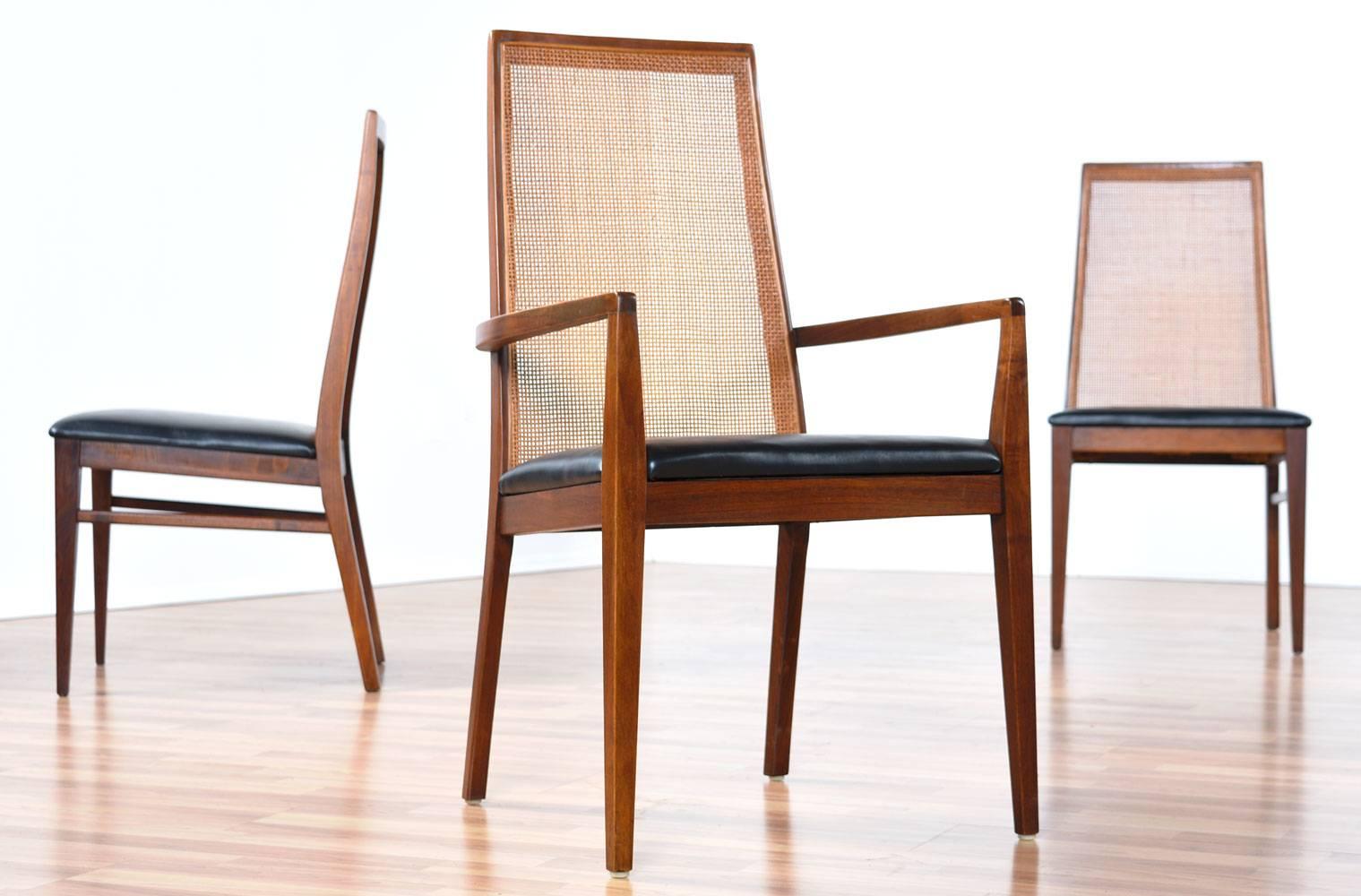 Set of six Milo Baughman for Dillingham walnut dining chairs. This set of six Mid-Century Modern chairs includes two captain's chairs with arms and four armless side chairs. Angled and sleek in design, walnut frames, rattan backs and black seats add