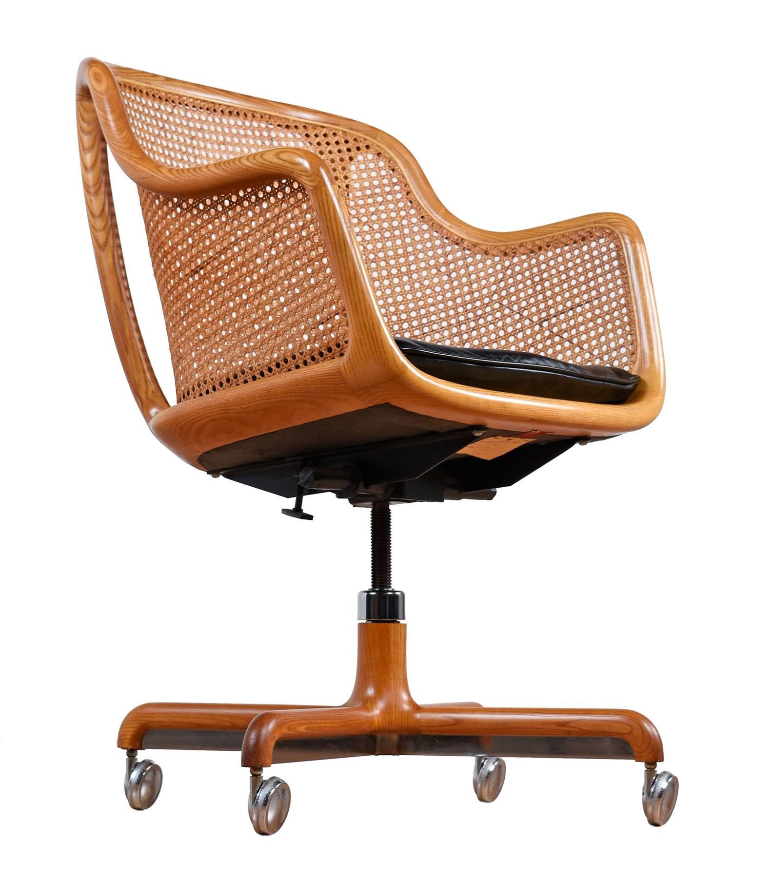 Gorgeous Mid-Century Modern cane desk chair by Ward Bennett for Brickel Associates. Made of ashwood, featuring a curved cane back and the original black leather seat. The chair is on wheels, the base tilts, swivels, and has a tension knob.

Arm