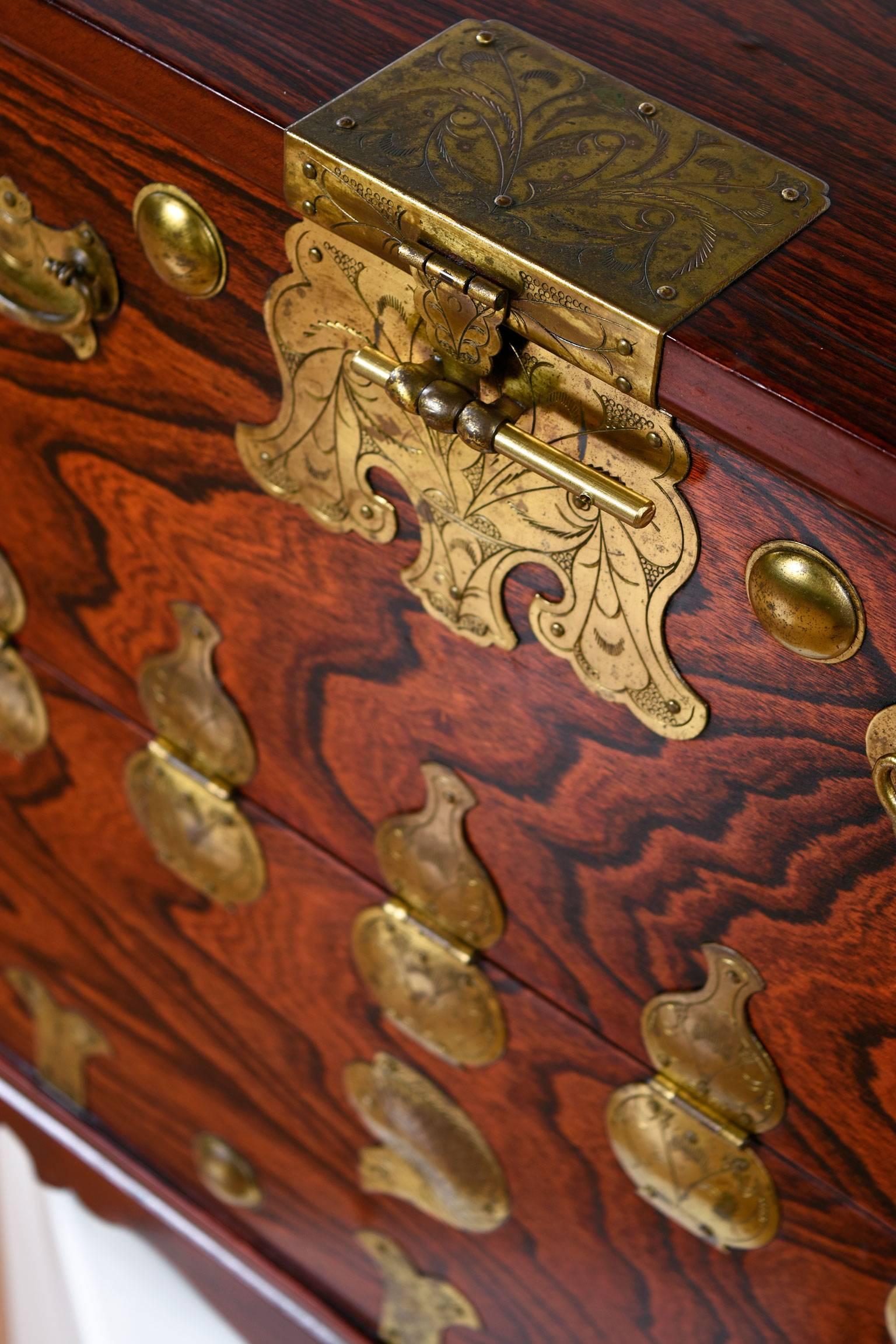 This unique, petite Asian chest is made of rosewood and decorated with ornate Korean brass. The combination of the rich wood grain and detailed brass ornaments give this small coffer an elegant old world feel. Front of the chest unlocks at the top