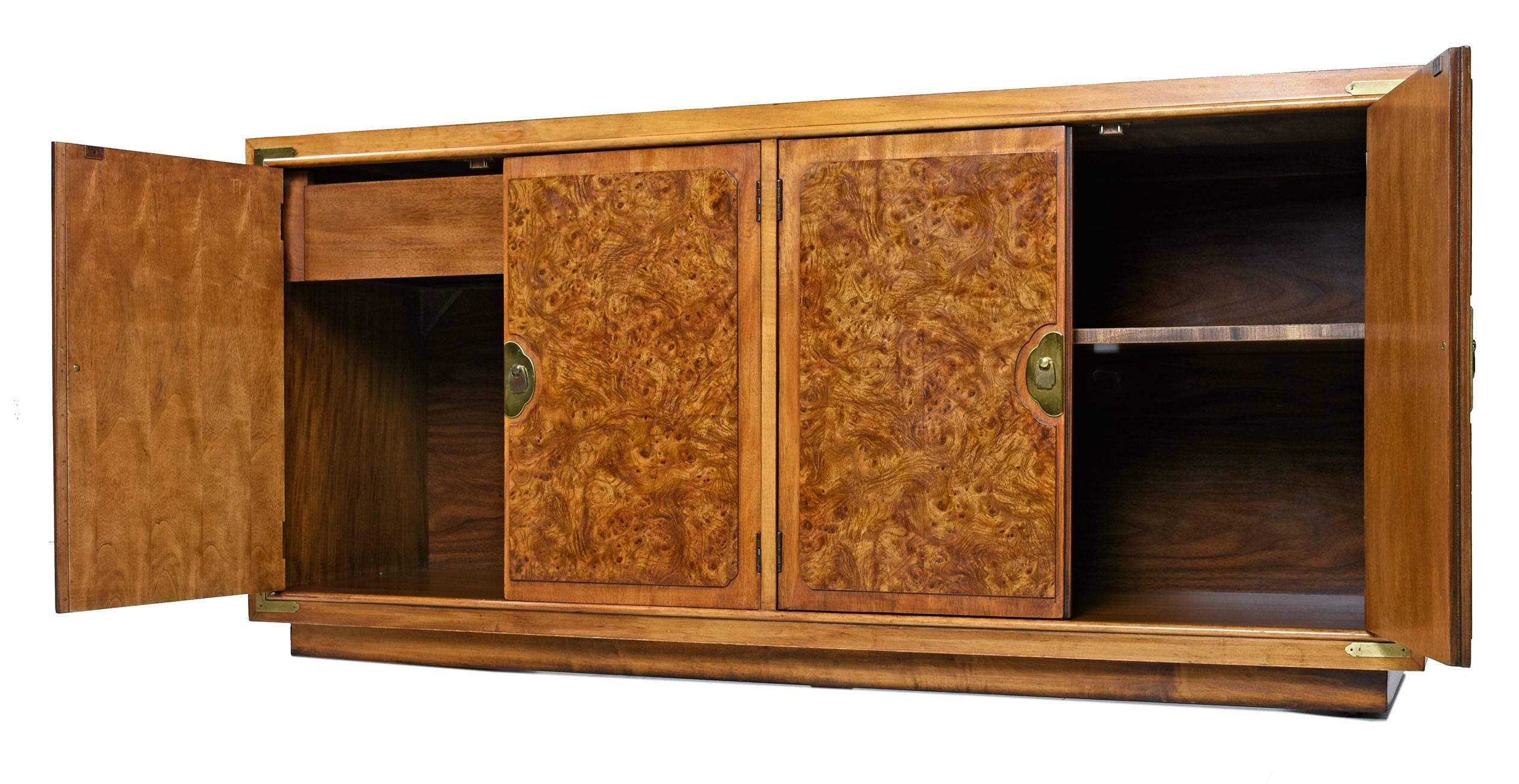 This impressive Asian inspired credenza by Thomasville, sits upon a solid wood pedestal base, and features burled wood cabinet door fronts. The two cabinets each have a simple yet elegant brass lotus shaped door pull and brass corner accents. This