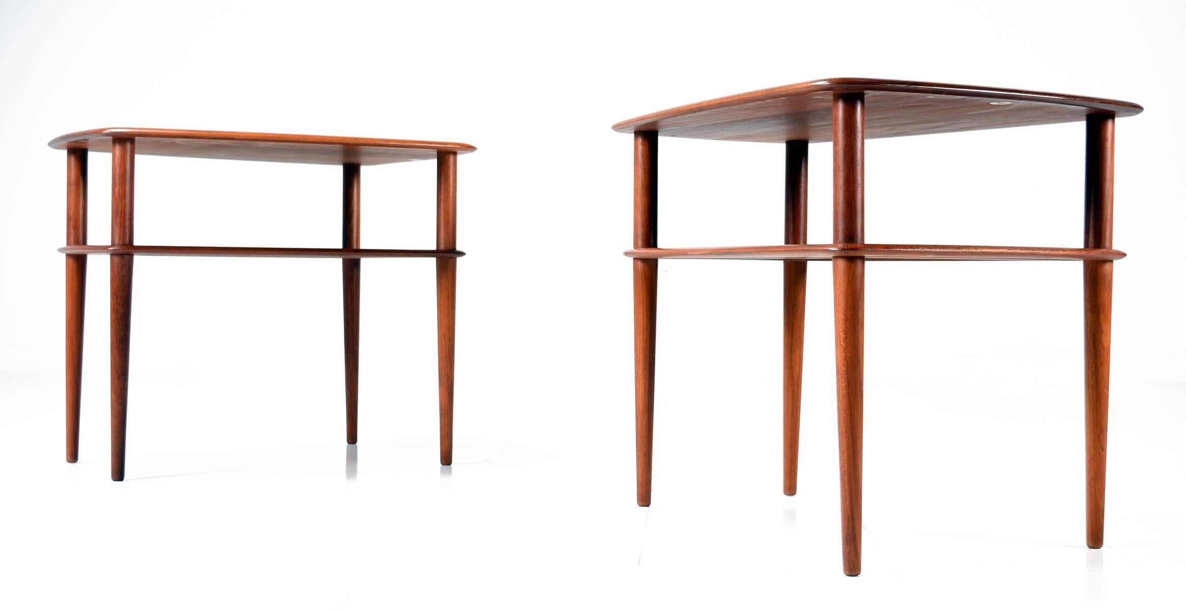 Pair of Mid-Century Modern solid teak end tables designed by Peter Hvidt and Orla Mølgaard-Nielsen for France & Sons. The lower shelves or magazine rack have the original caned inserts, surrounded by solid teak frame. The pair are a trazezoid shape,
