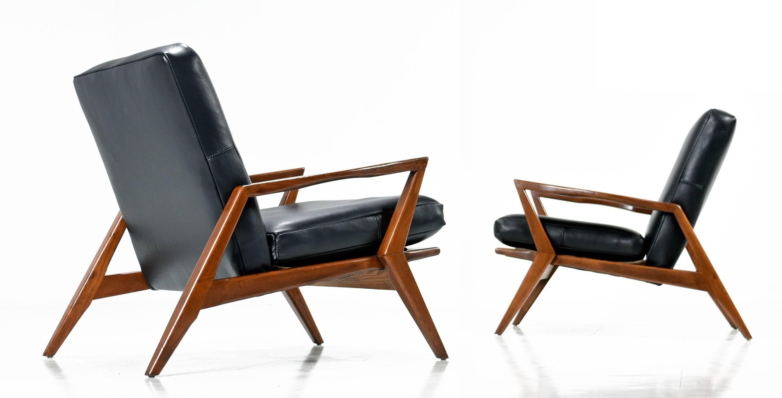 Stunning pair of Mid-Century Modern armchairs restored in new full grain black leather upholstery. American made, vintage 1960s, this handsome pair cuts a wicked Silhouette with the sharply angled "Z" shaped arms and legs. The solid walnut