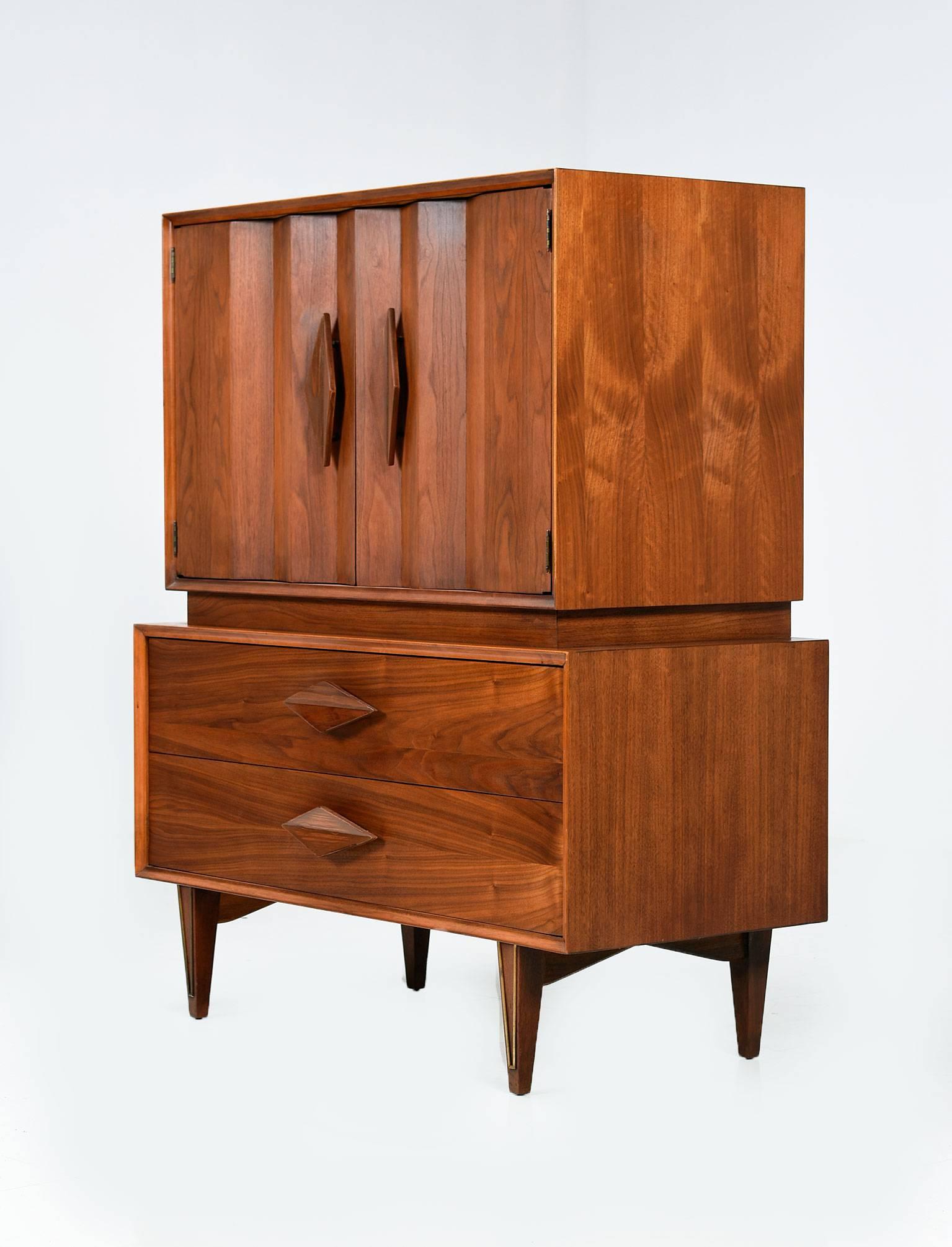 Mid-Century Modern American made walnut Gentlemans Dresser Highboy. This stunning walnut dresser features sculpted diamond shaped drawer pulls and brass detailing along the front of the legs. The top cabinet opens up to reveal three drawers which