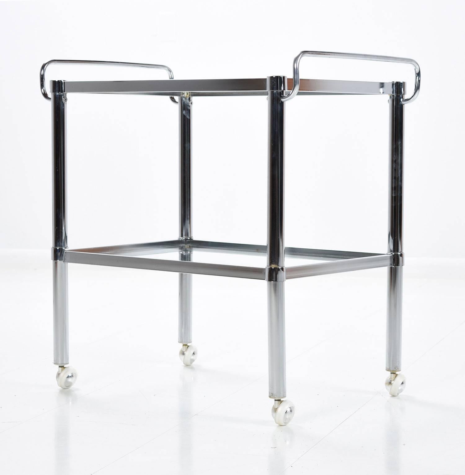 Mid-Century Modern chrome and glass bar cart, circa 1960s. The cart is in the Milo Baughman features two levels of glass shelves and rolling casters. The piece is completely original. Our team of professionals have hand polished the chrome. Light