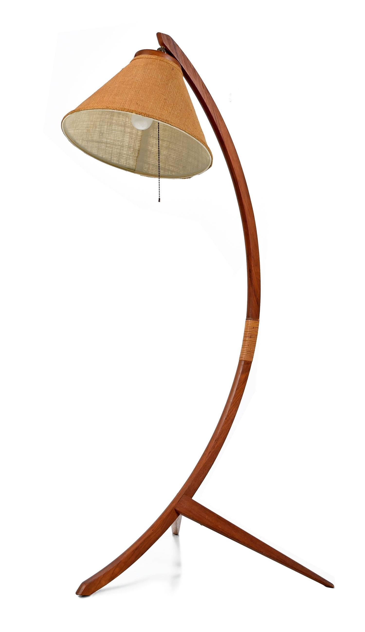 Iconic Mid-Century Modern Danish teak floor lamp in the style of Rispal, is all original, made in the 1960s. This solid teak floor lamp features a gorgeously sculpted bow shaped stem, resting on a tripod base, the articulating lampshade suspended