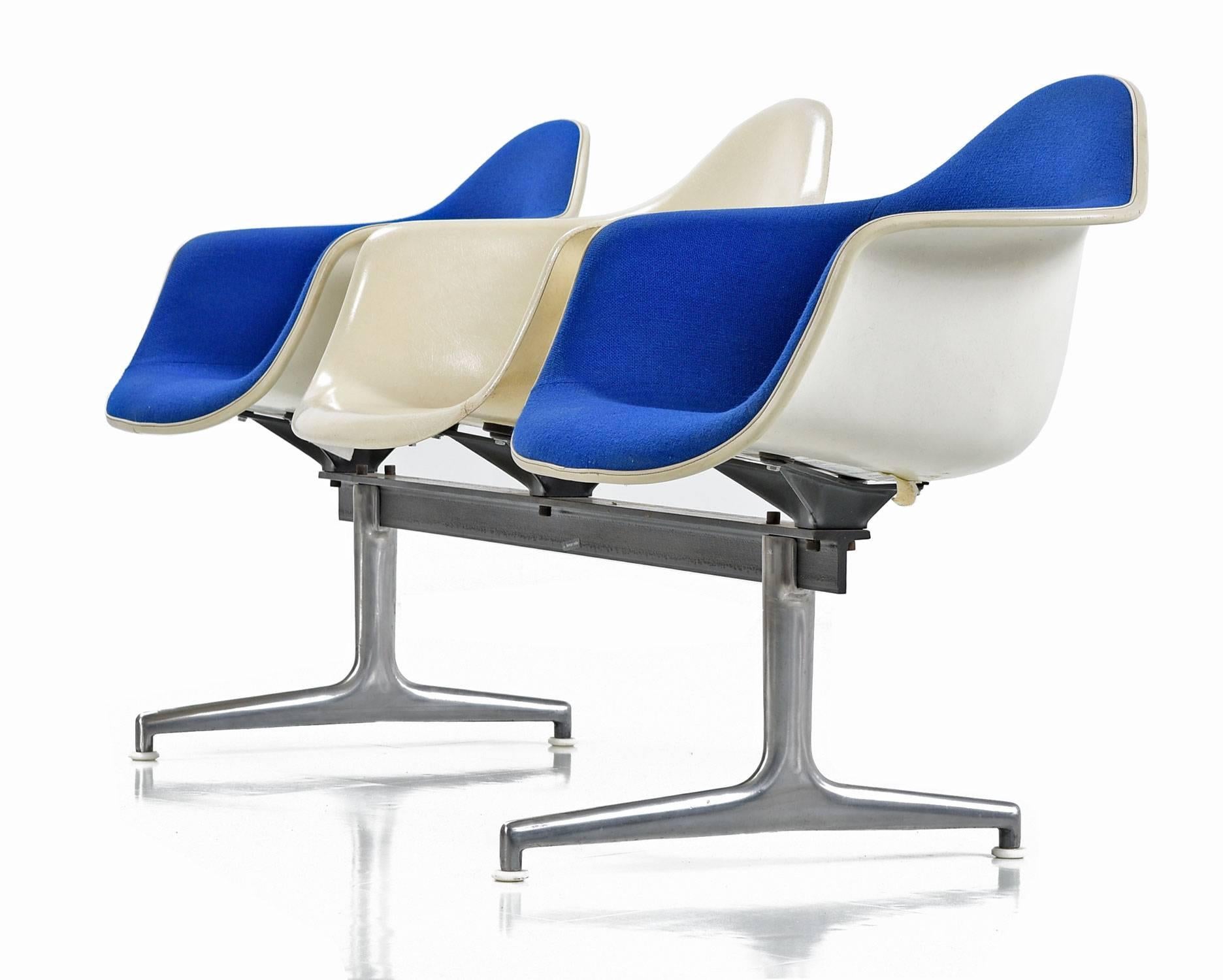 (Two) Shell chairs seats in original blue fabric and (one) off-white fiberglass seat positioned in the center sit atop a metal and aluminum frame. Originally used in commercial settings, this Industrial grade bench can be seamlessly integrated in a