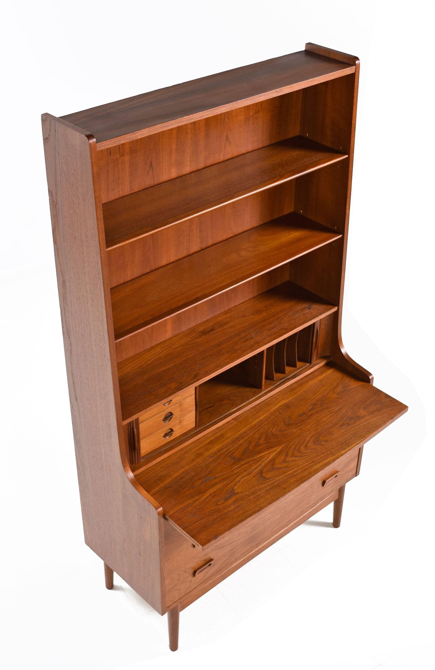 Exquisite Danish made bookcase with secretary desk. The piece packs a wallop with storage capability. Store books and collectibles on the upper bookcase, private storage with divided compartments are concealed behind the tambour doors at center.