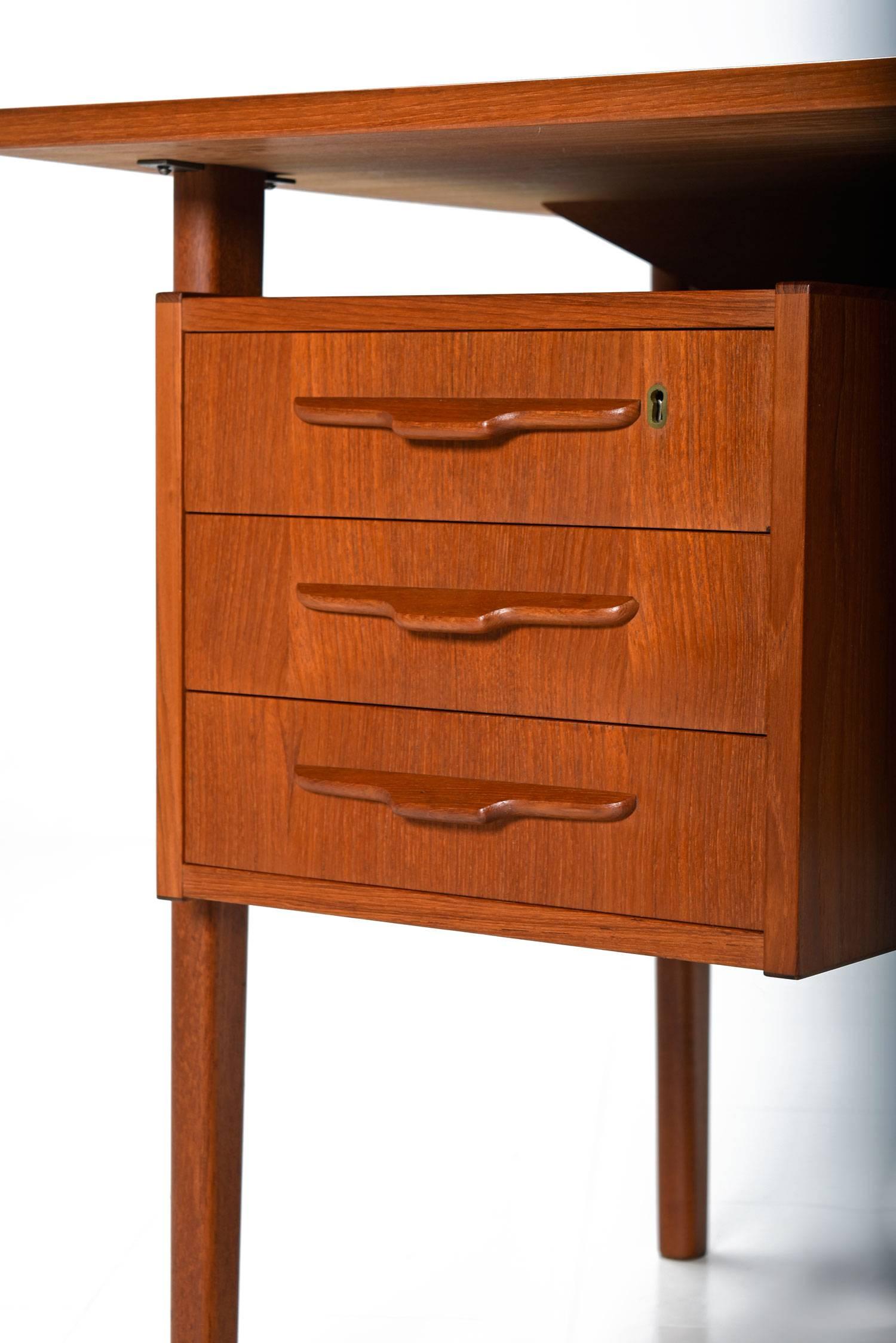 Mid-Century Modern Danish teak desk with plenty of storage via six drawers on the back and two bookcase spaces on front. The desk features a locking drawer (key included). The unique front side has bookcase storage spaces flanking the center. Expert