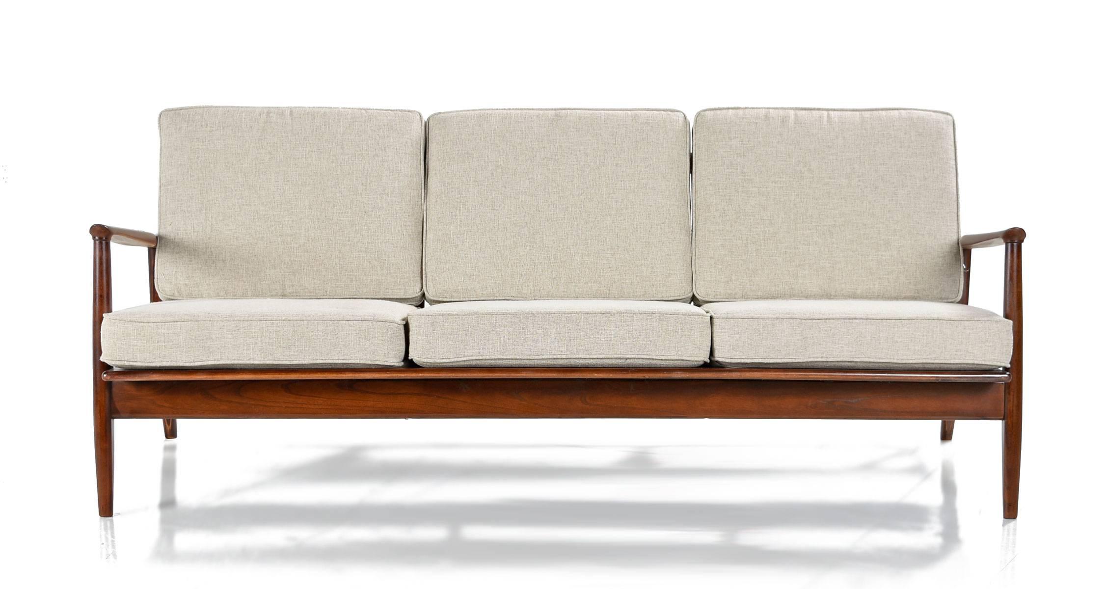 Retro Eames era sofa with Danish modern styling. Note the remarkable subtle detailing in the wood frame. Angled back legs add visual dynamism. This angle gives a gentle reclined position to the couch, enhancing comfort. The wide, sculpted arms taper