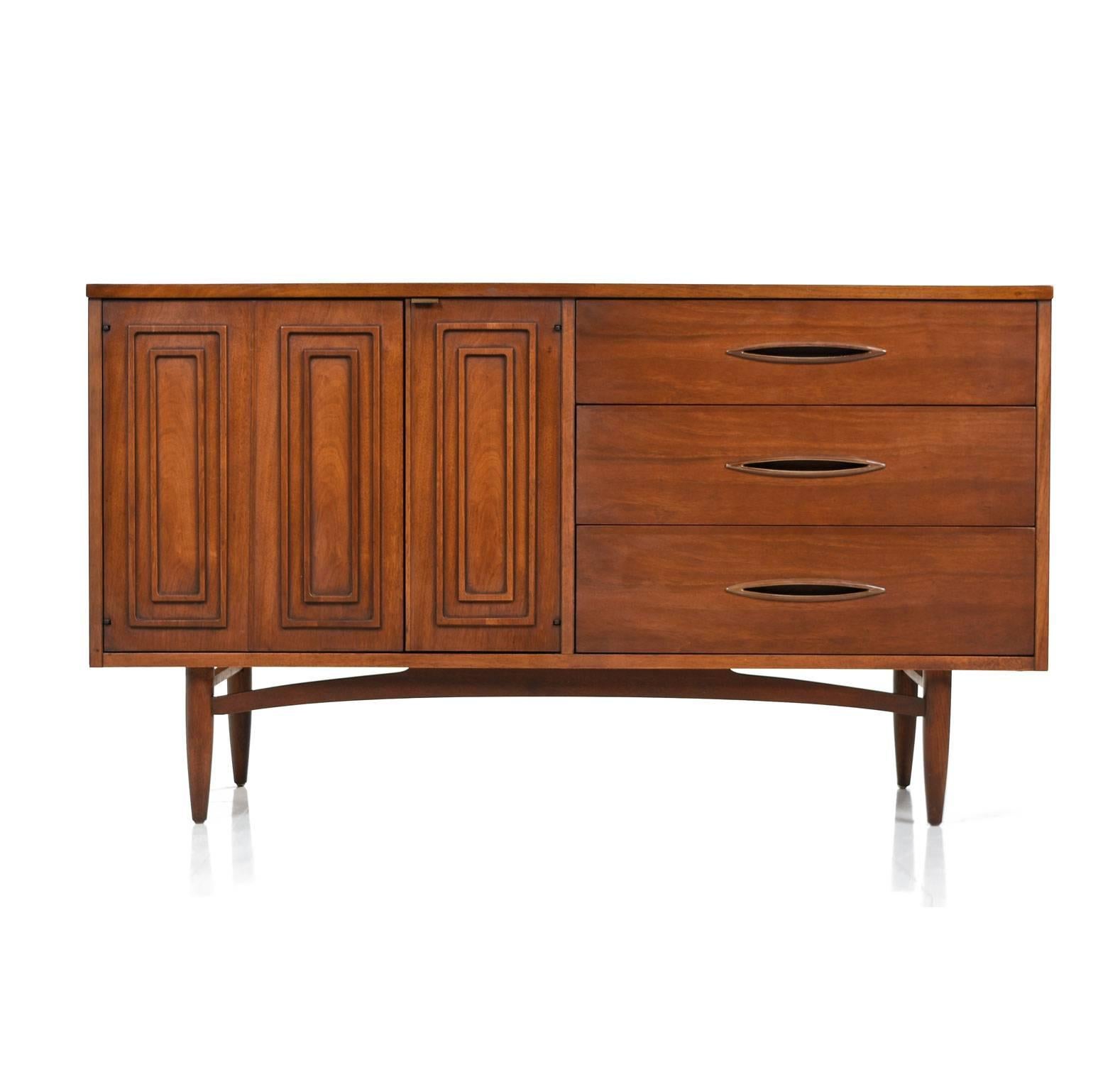 Mid-Century Modern sculptra credenza by Broyhill. Signature relief cut pattern adorns the cabinet doors. Inset elliptical handles on the drawers enhance the atomic age charm. Left side features a cabinet space. Additional storage to the right with