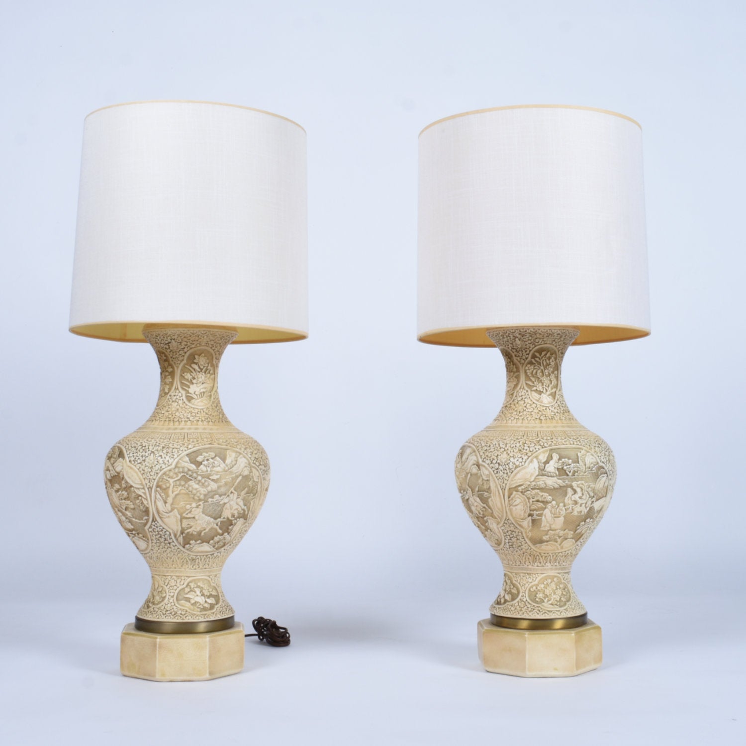 A savory patina enriches the bone colored vintage carved Asian chalkware lamps. Each bit of these lamps were ornately decorated with carved Oriental botanical and figural elements. A series of medallions decorate the mid-section, depicting scenes