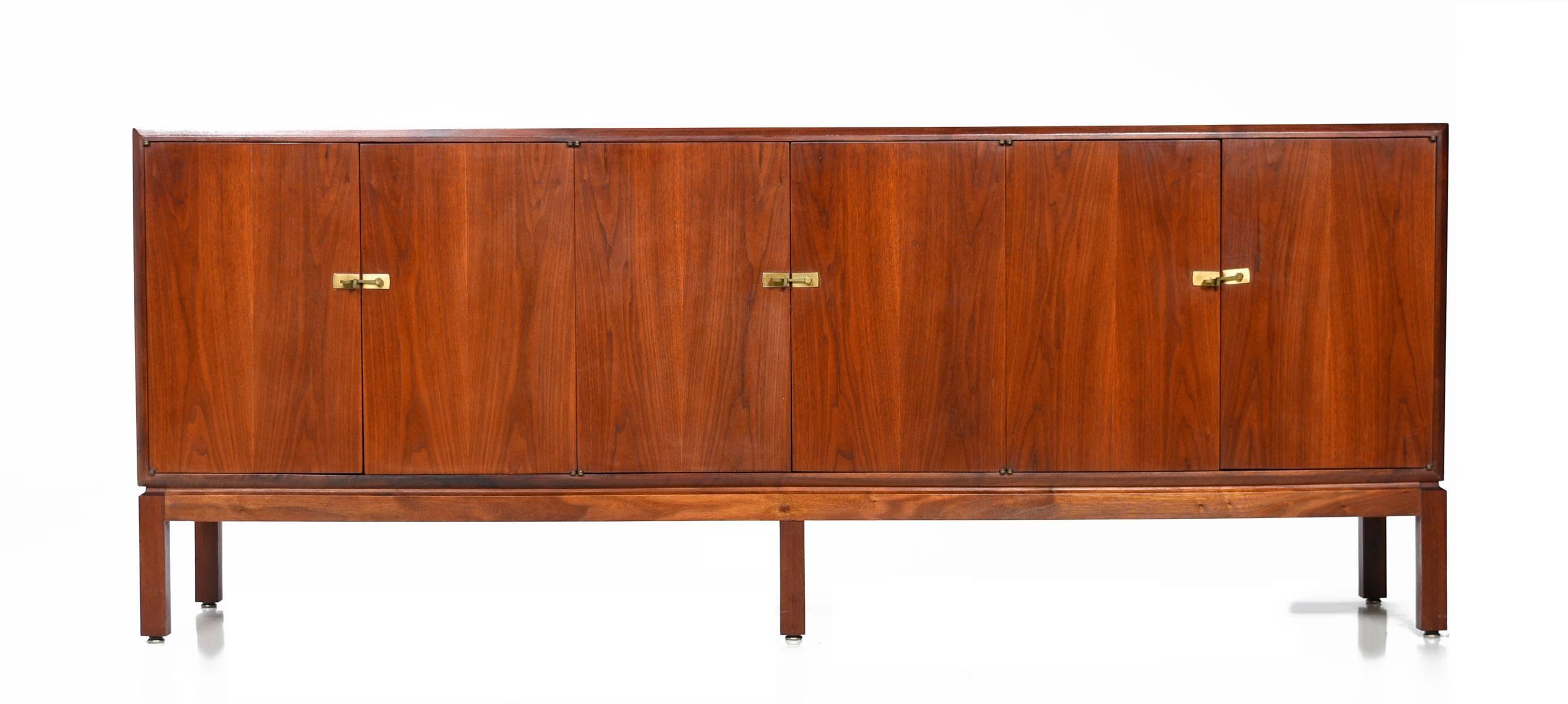 Restored Mid-Century Modern American made walnut credenza. The simple design is embellished with brass latches along the door fronts. This piece is intriguing in the way that it balances modern and traditional themes. The exceptional length is the