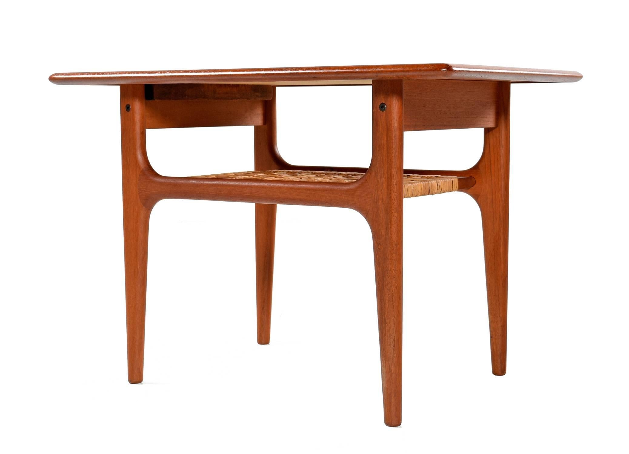 Refinished Mid-Century Modern Danish teak end table by Trioh Møbler. Two-tier design with a cane lower shelf. The original weaving is amazingly still intact! The end table exhibits smart styling with sharp architectural profile tempered by graceful