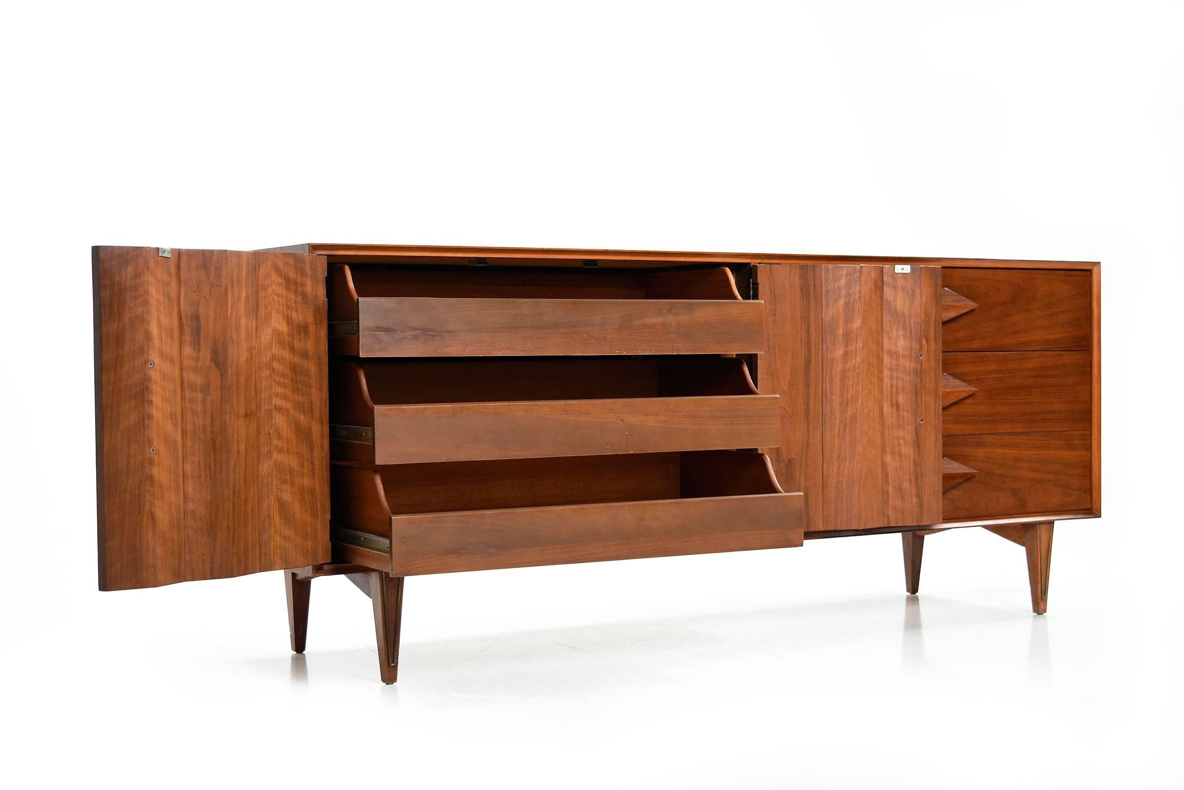 Mid-Century Modern walnut double dresser, made in America in the 1950s. This stunning double dresser features walnut sculpted diamond shaped drawer pulls and brass detailing along the front of the legs. This well designed and beautifully crafted