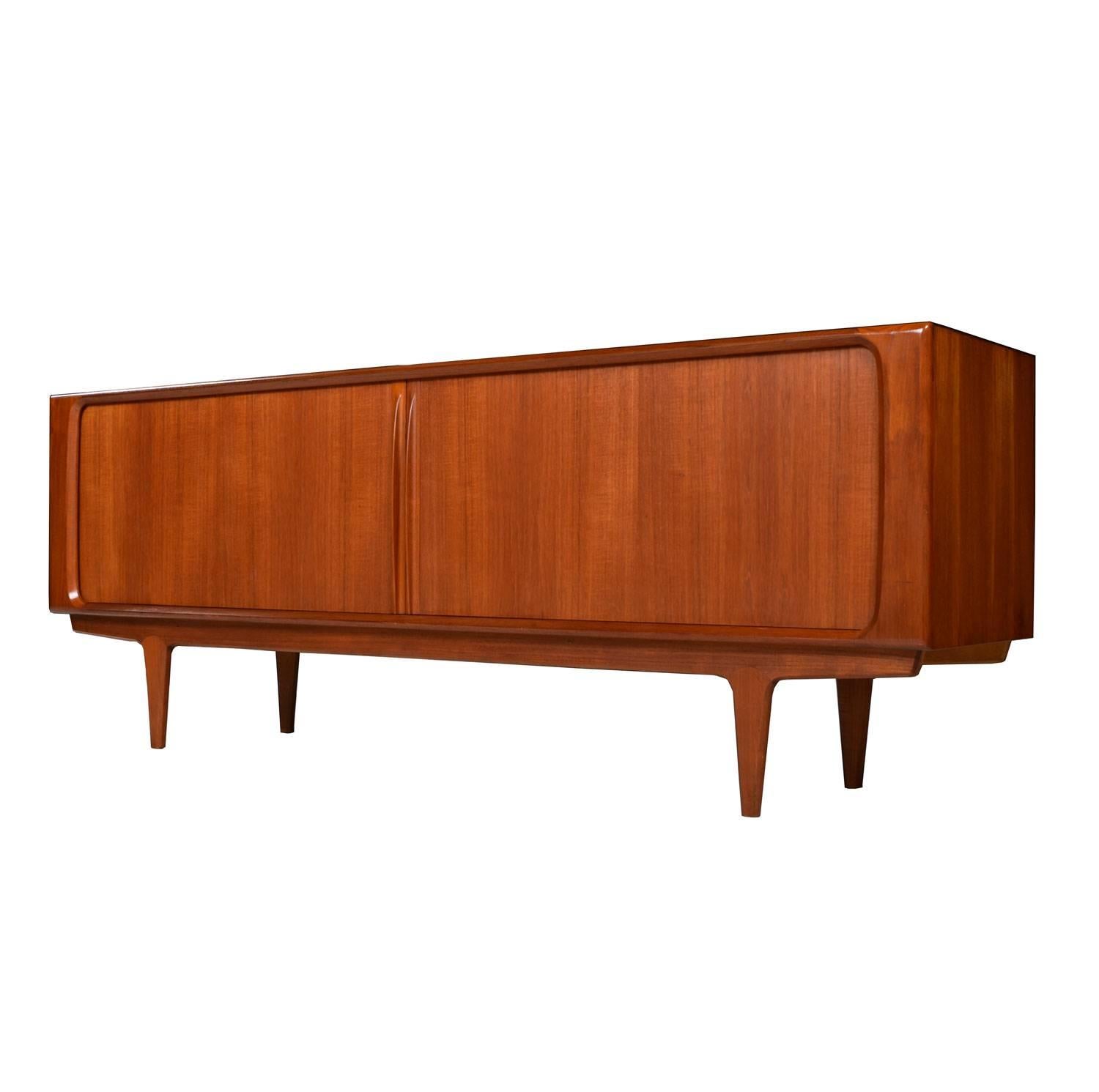 Long Mid-Century Modern Danish teak credenza by Bernhard Pedersen. Expertly crafted with sleek lip-like, solid teak carved handles gracing the tambour doors. Open the cabinet to reveal cabinet space at left and right. A stack of three drawers reside