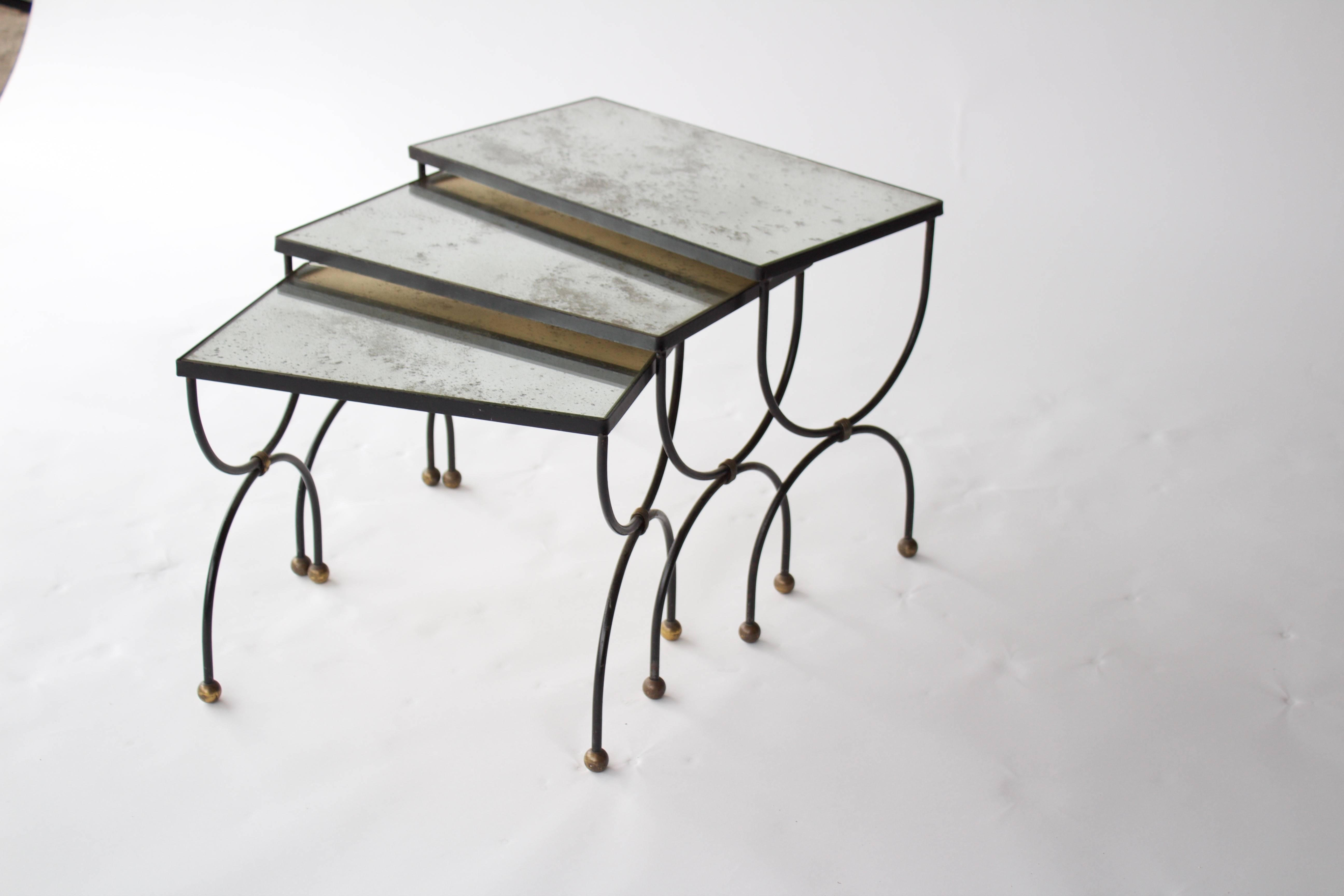 A set of three nesting tables from Mid-Century, France. Each table has an iron base, brass ball feet, and an antiqued mirror top.