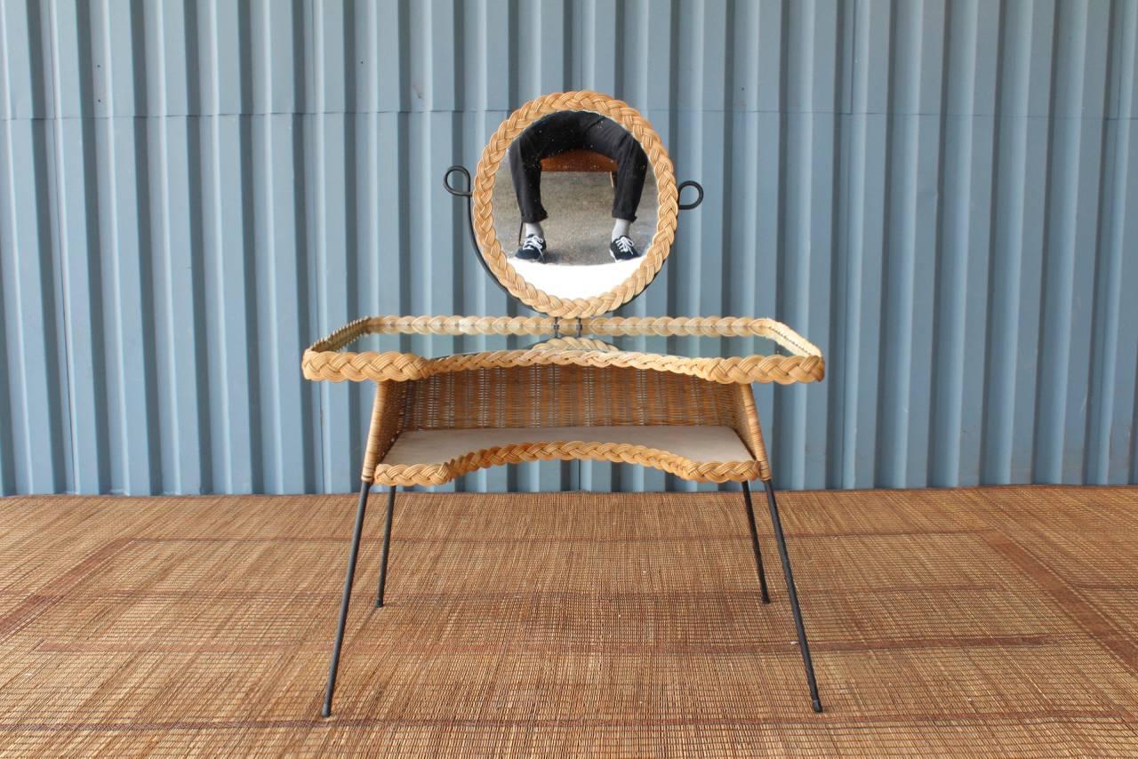 1950s French vanity made of woven rattan (wicker) and iron. Features an antiqued mirrored top, lower shelf and a swiveling vanity mirror.