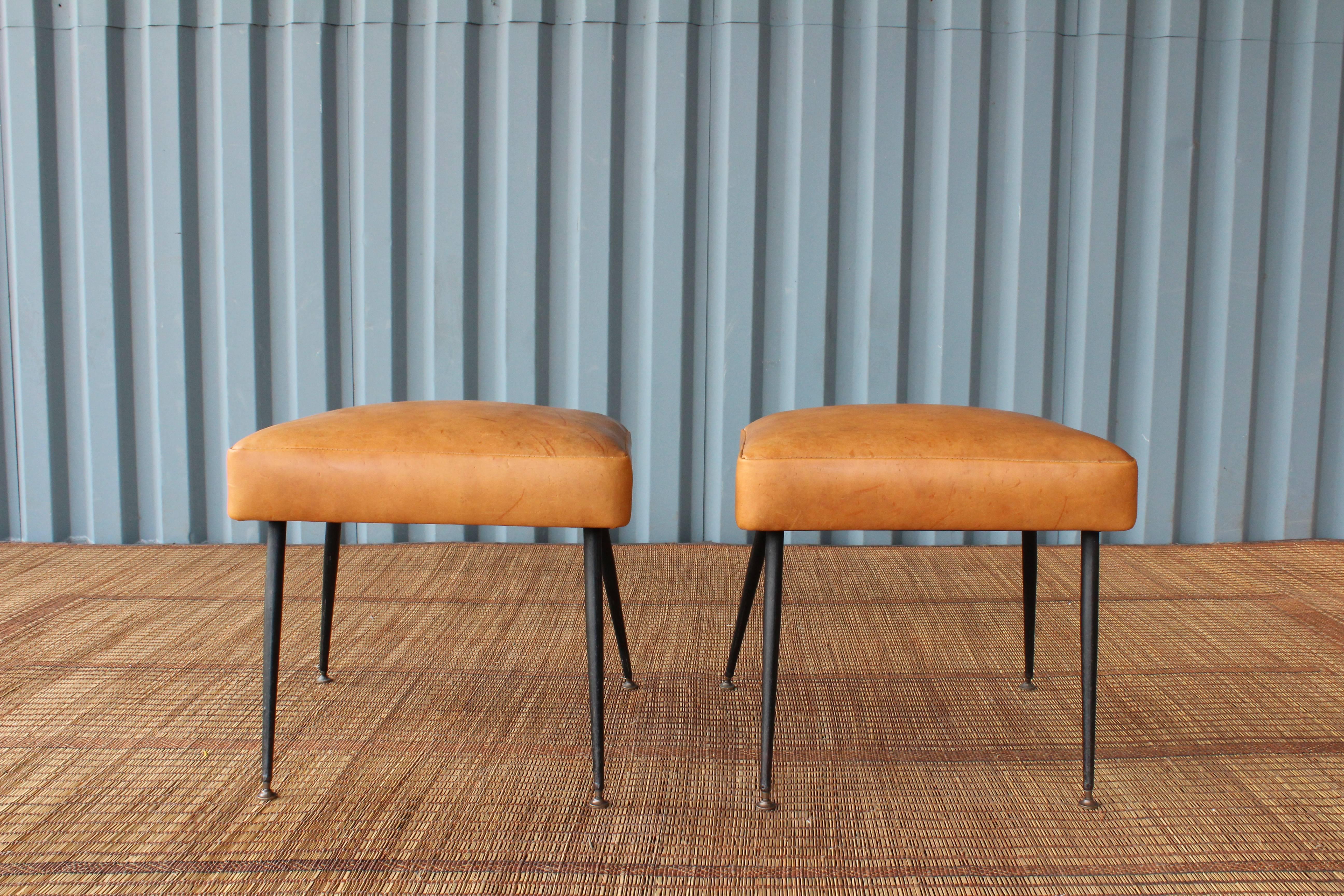 Sleek pair of 1950s Italian modern footstools. Steel legs with brass pivoting feet. Recently reupholstered in soft vintage leather hide.