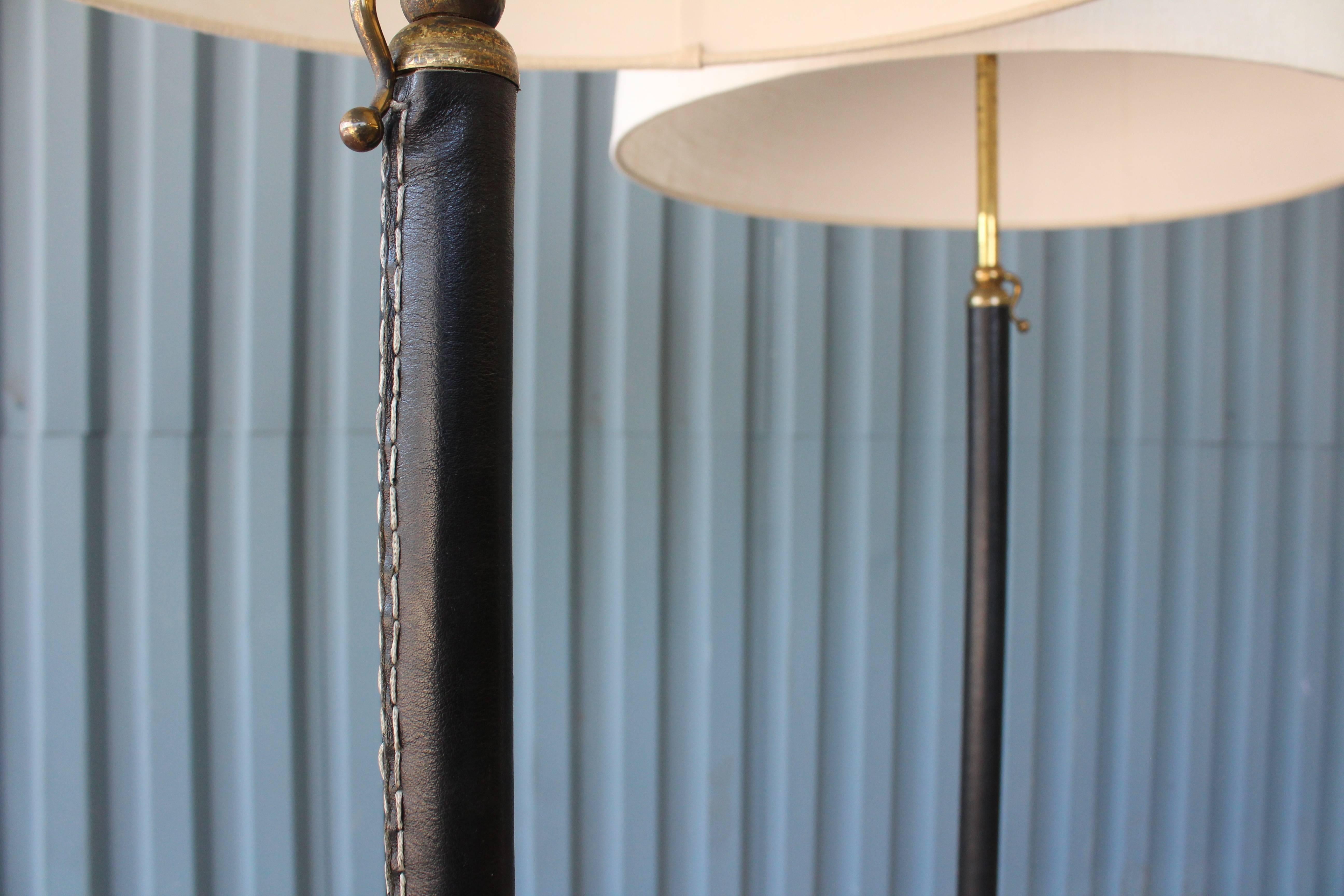 A stunning pair of 1950s leather wrapped floor lamps in the manner of Jacques Adnet, France. The pair are both height adjustable and have been newly rewired for U.S standards. Custom linen shades included.